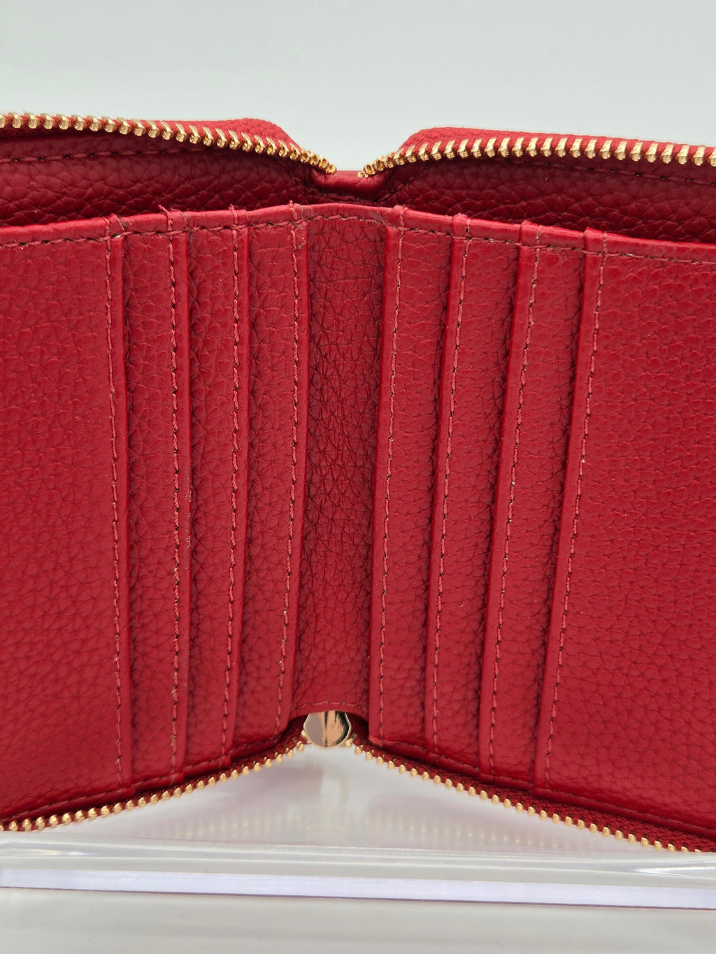 Red pebbled leather zip-around wallet shown open, displaying multiple vertical card slots, interior stitching, and gold-tone zipper hardware.