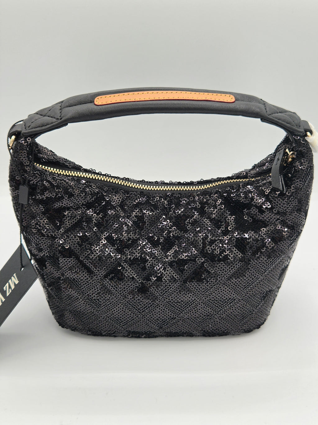 A black sequined crescent-shaped shoulder bag with a top handle, gold-tone zipper, and a black branded hangtag, photographed on a light gray background.