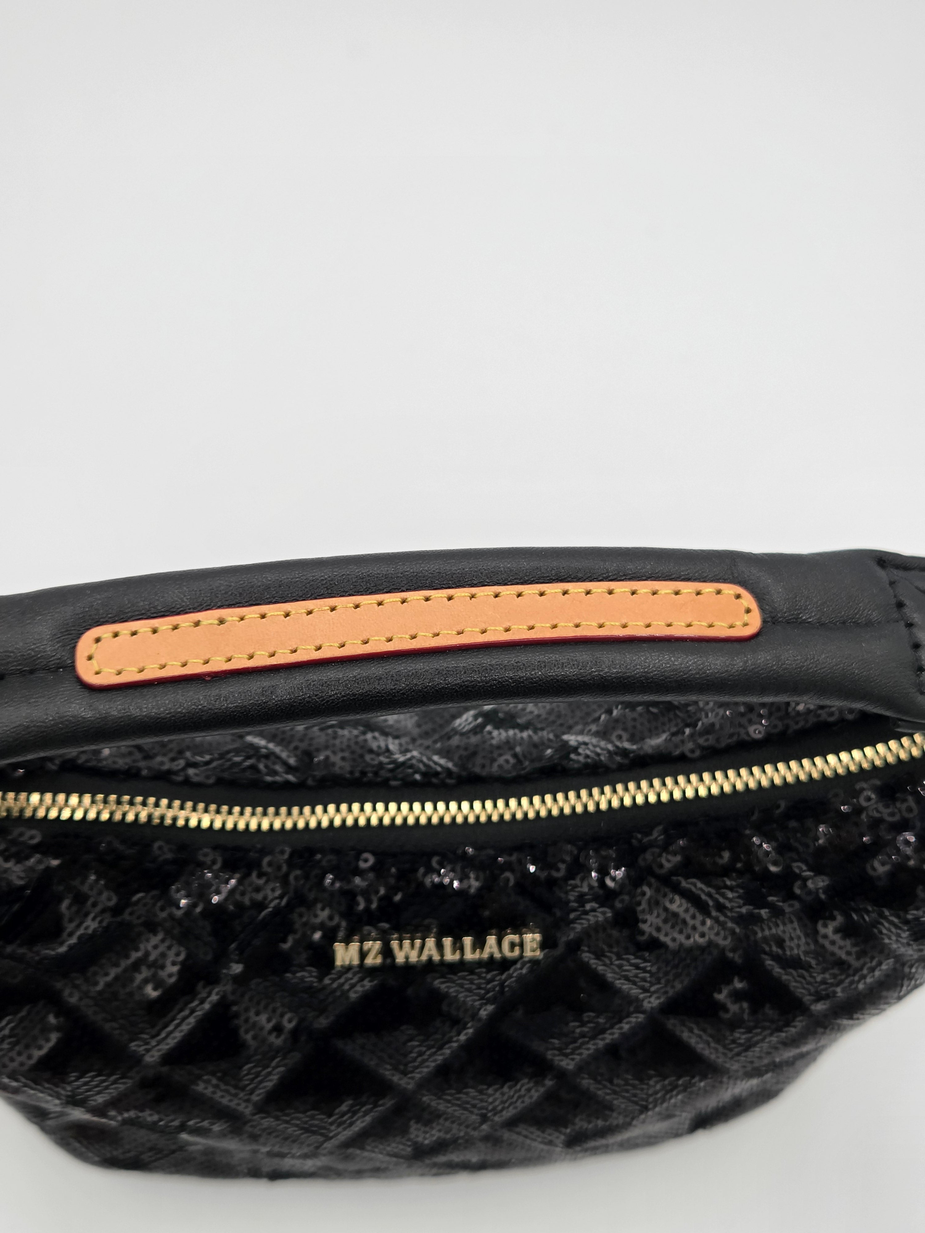 Close-up of a black quilted fanny pack with a gold zipper, a tan leather trim, and the brand name 'M2 WALLACE' in gold lettering.