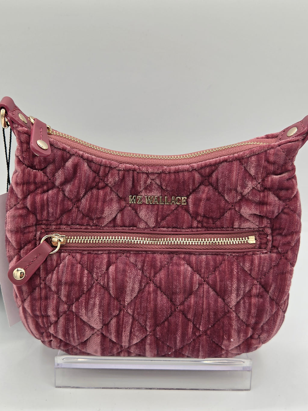 A quilted dusty rose velvet shoulder bag with gold-tone hardware and a visible 'KE WALLACE' logo on the front, displayed on a clear acrylic stand against a light gray background.