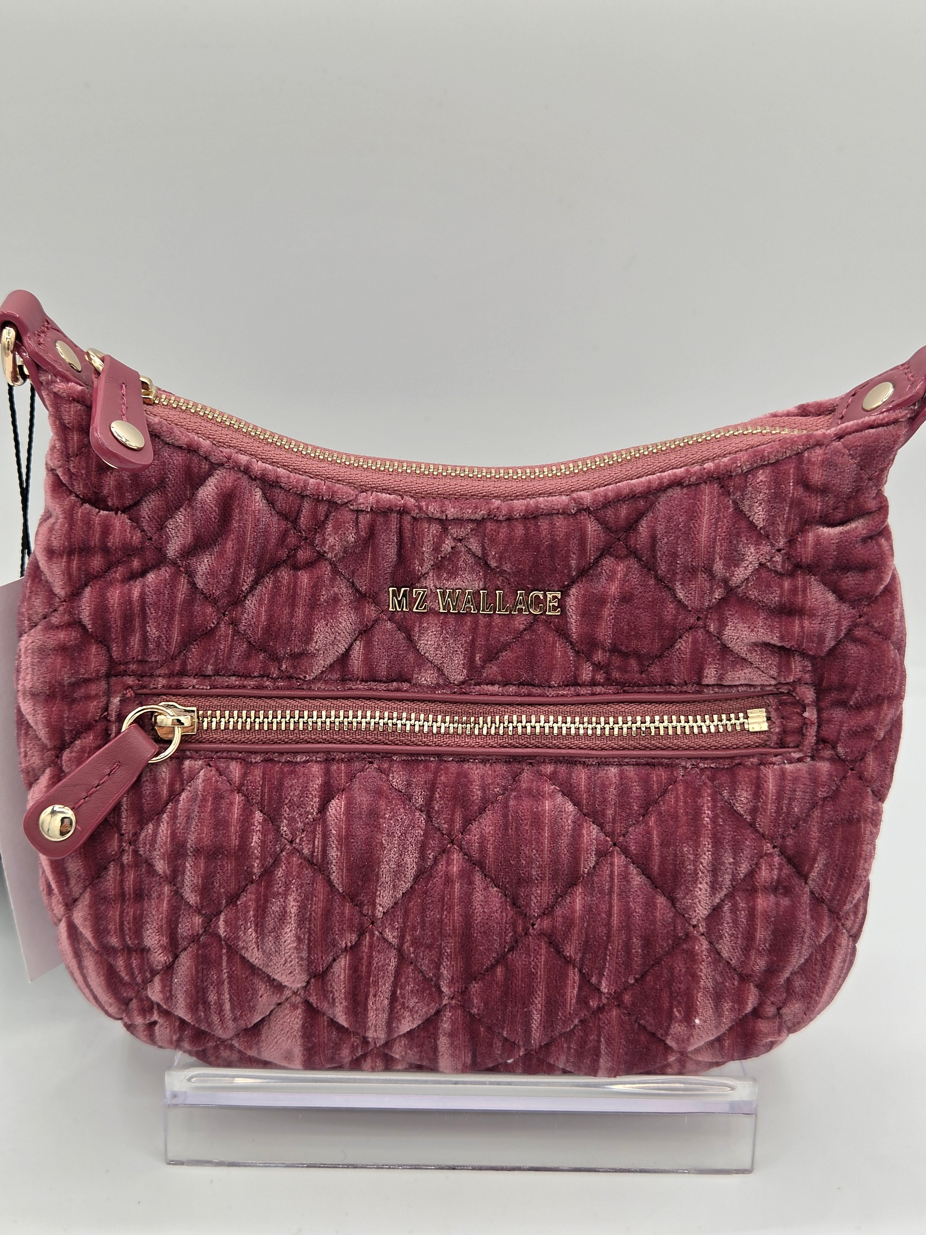 A quilted dusty rose velvet shoulder bag with gold-tone hardware and a visible 'KE WALLACE' logo on the front, displayed on a clear acrylic stand against a light gray background.