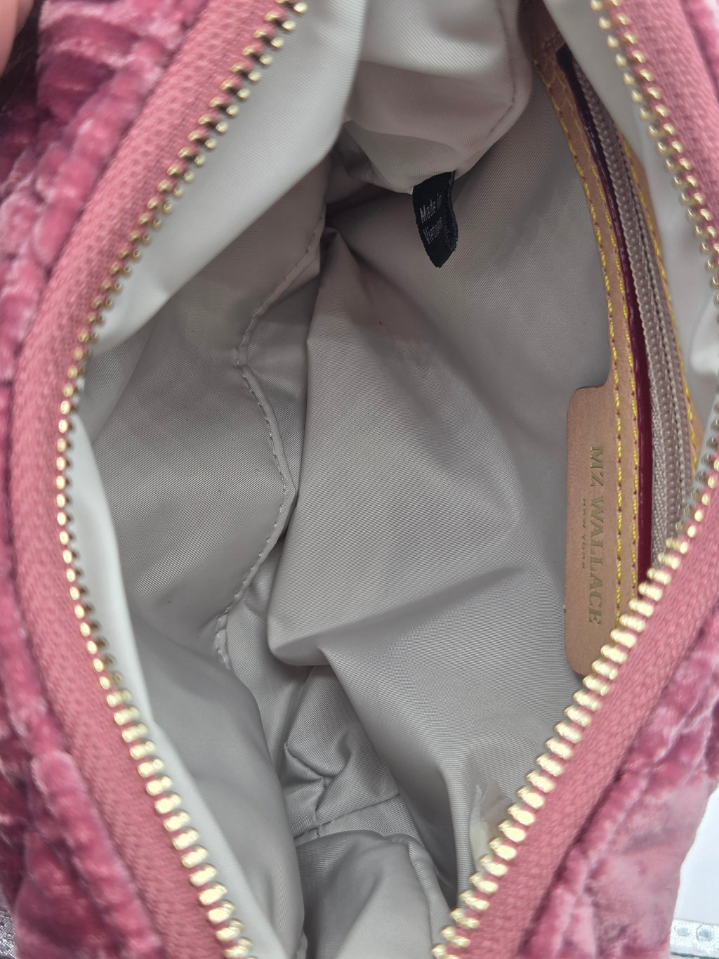 Close-up of the interior of a pink velvet zippered bag, showing a light gray nylon lining, gold-tone zipper teeth, and a tan leather brand tag that reads 'MIA WALLMACKER'.