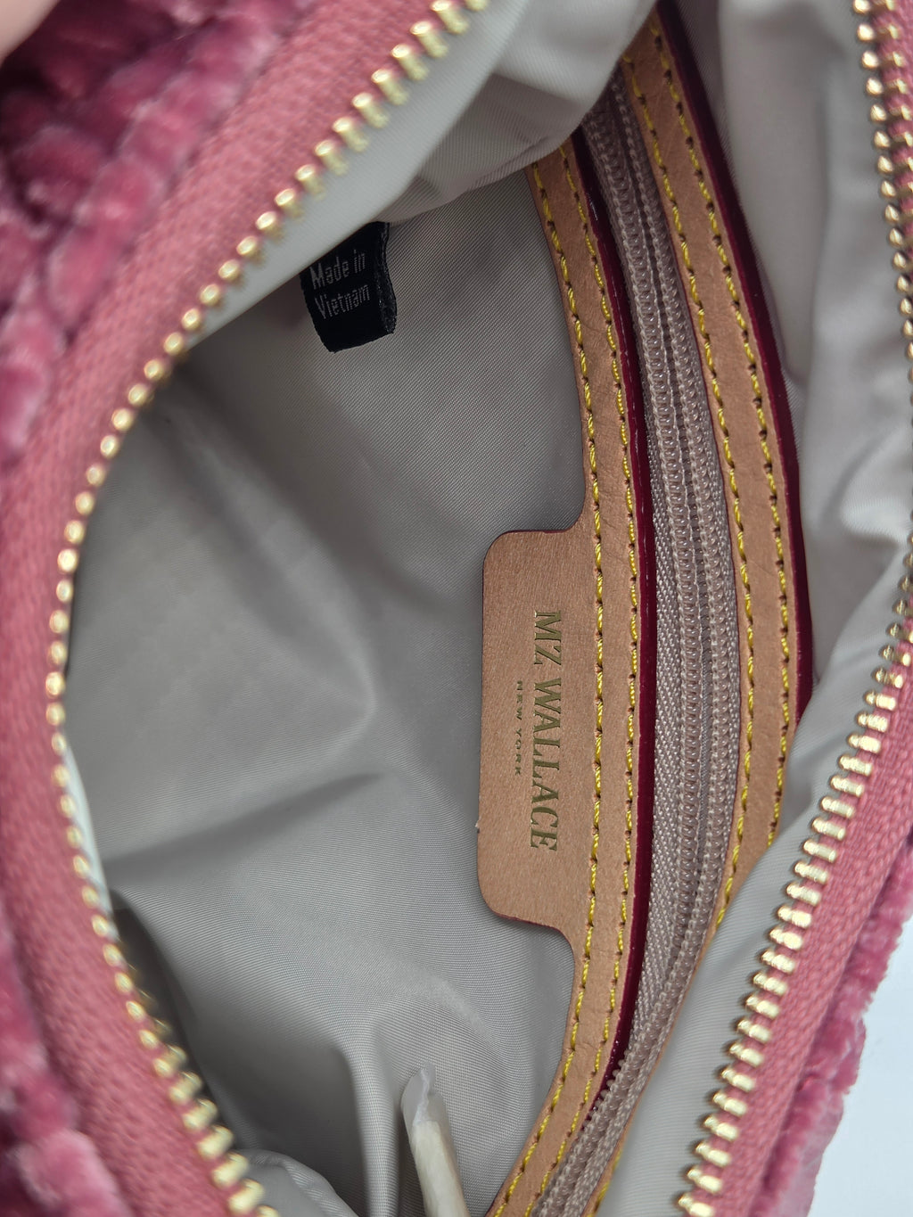 Close-up of the interior of a pink textured handbag, showing a light gray lining, gold-tone zipper, and a tan leather brand tag reading MW WALLACE.