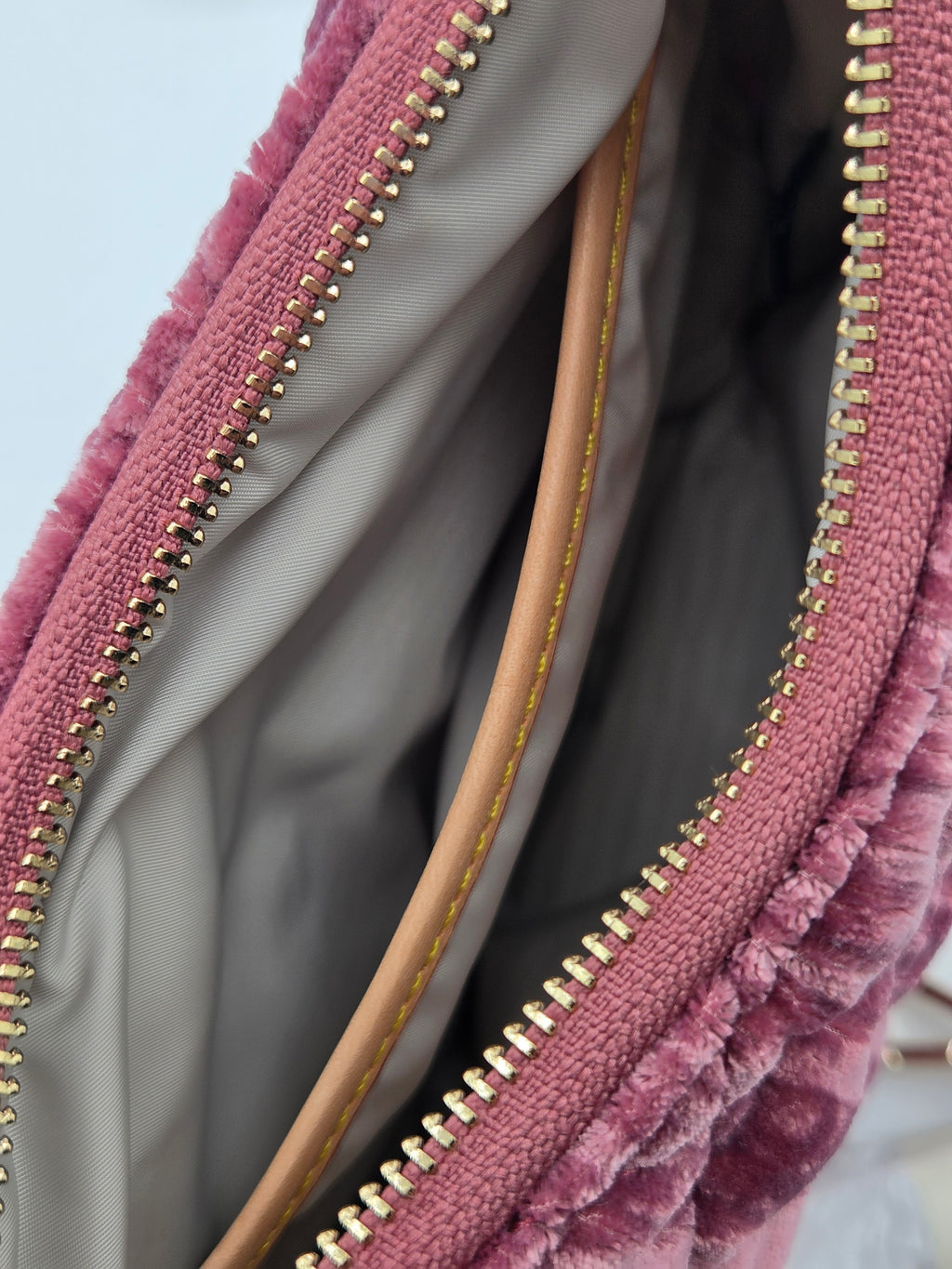 Close-up of a dusty pink textured velvet bag with gold-tone zippers and a light beige interior lining.