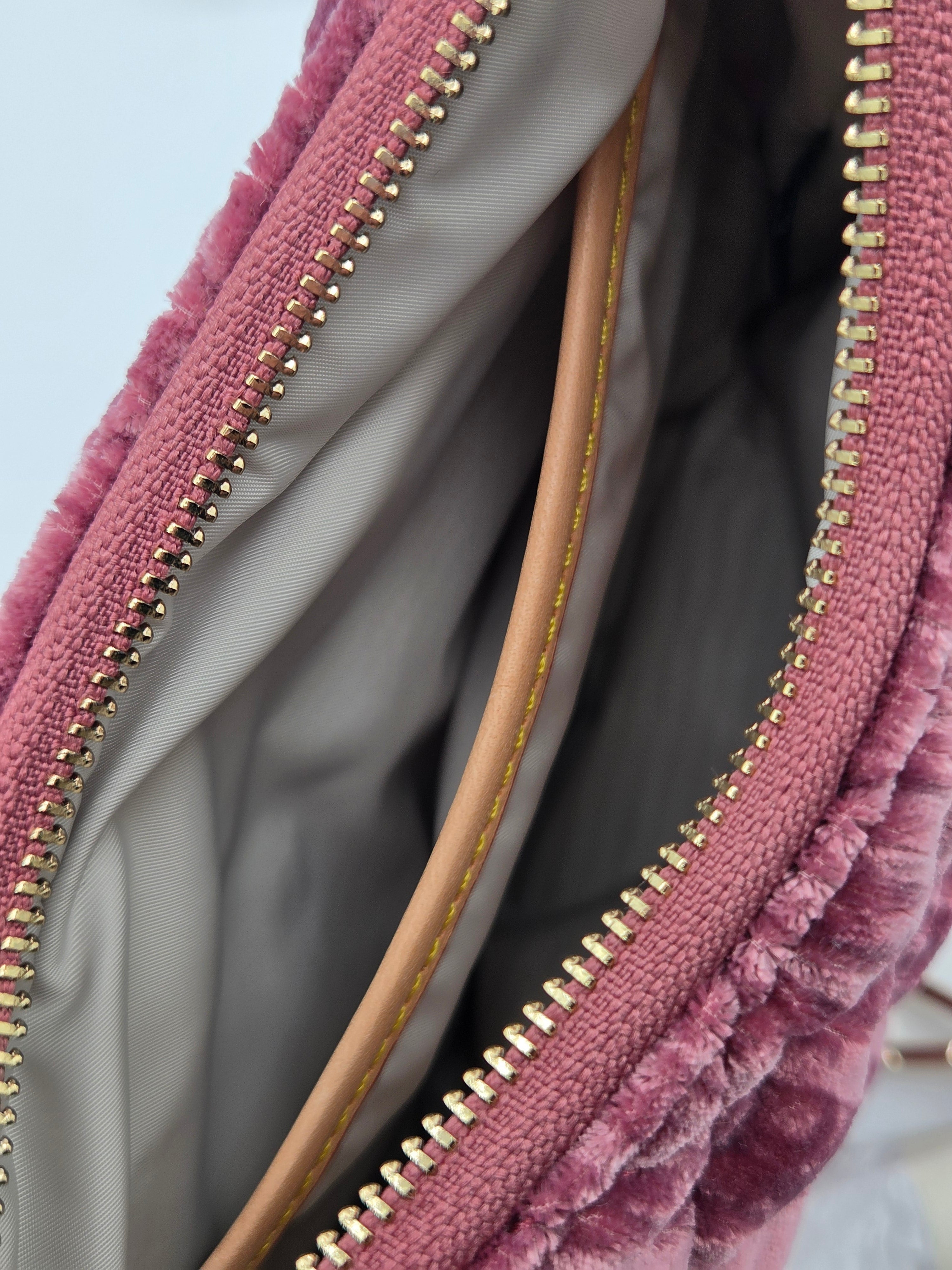 Close-up of a dusty pink textured velvet bag with gold-tone zippers and a light beige interior lining.