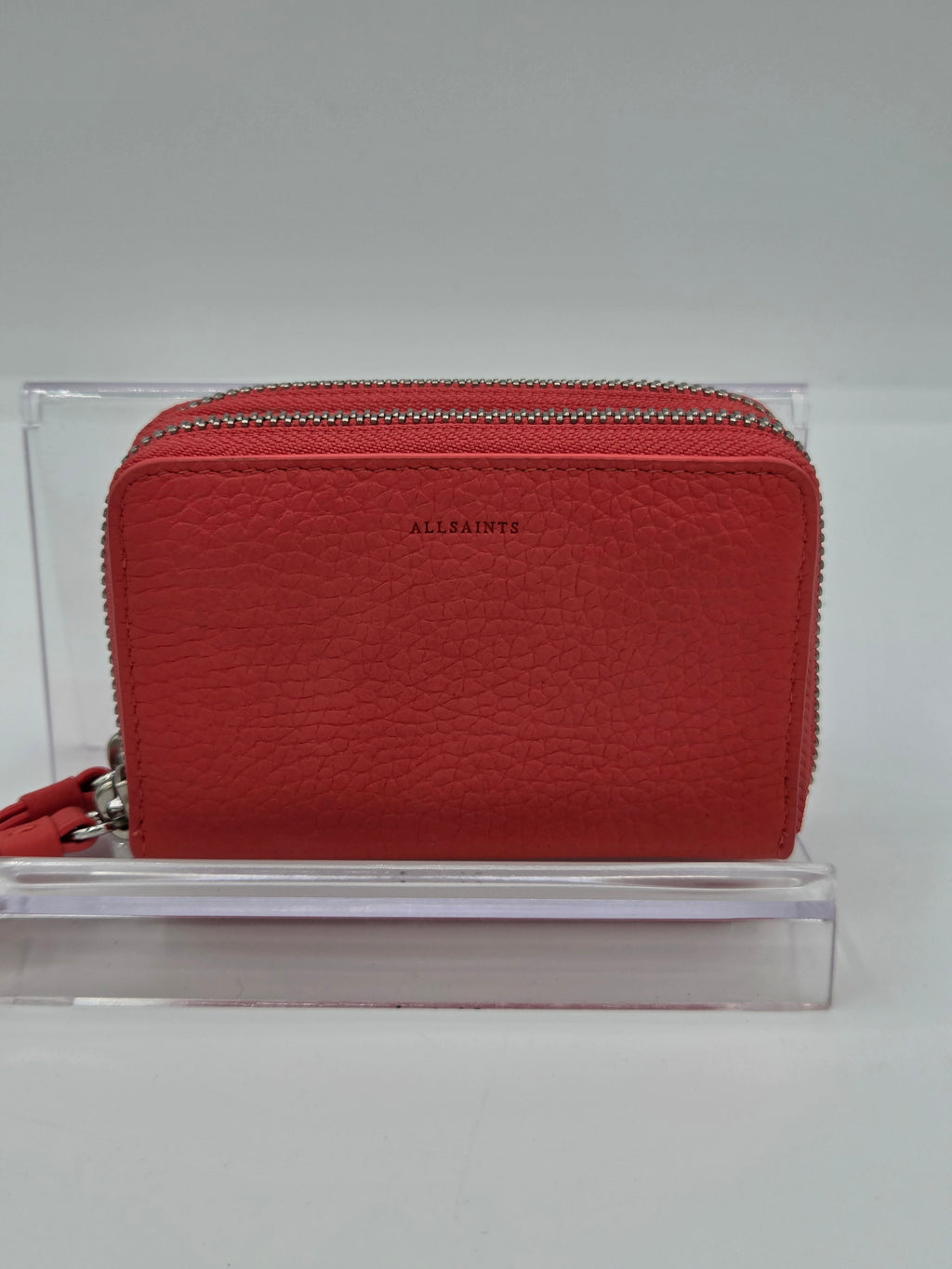 A red textured leather zip-around wallet by Allaints, displayed on a clear acrylic stand against a neutral gray background.