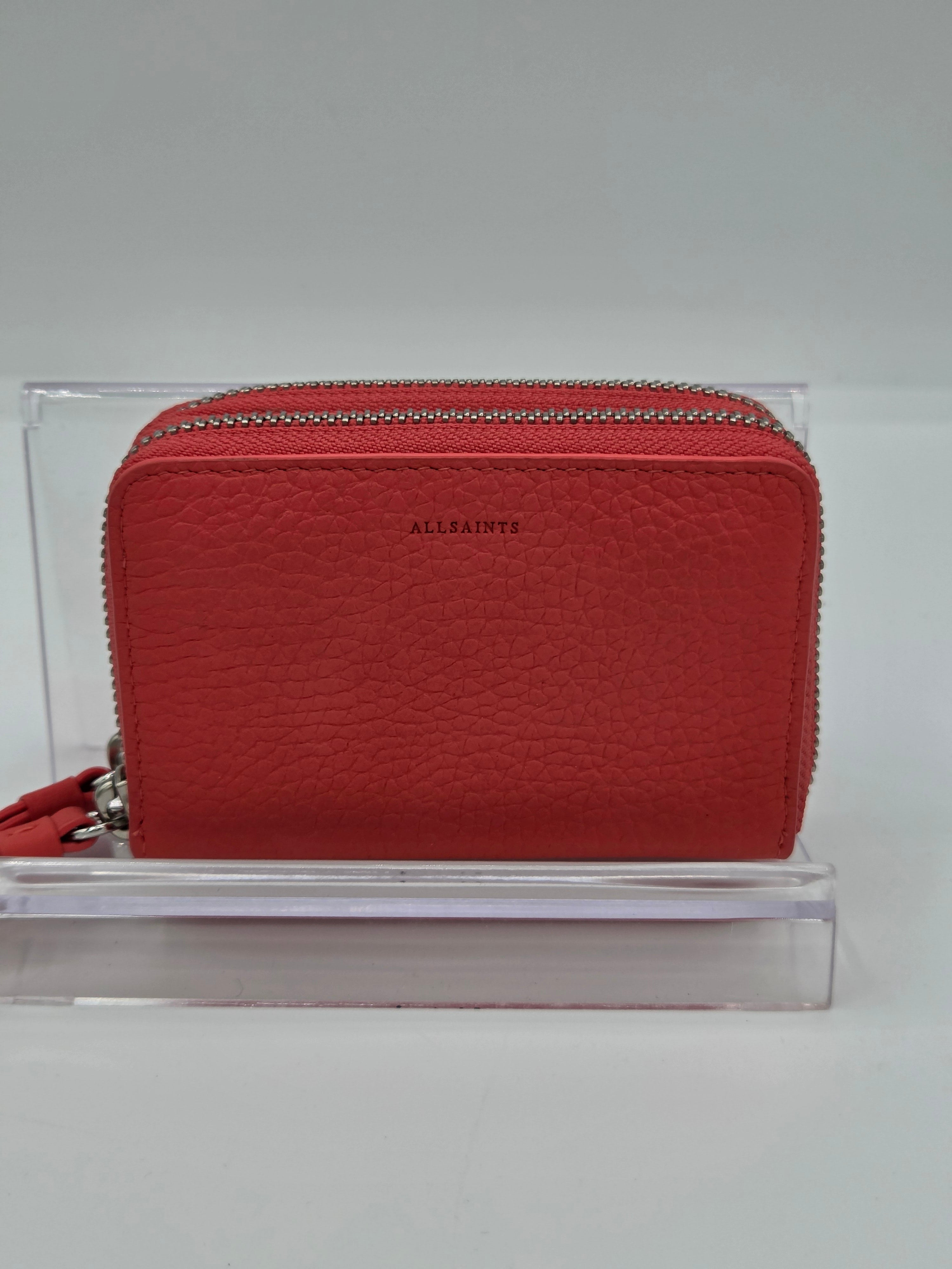 A red textured leather zip-around wallet by Allaints, displayed on a clear acrylic stand against a neutral gray background.