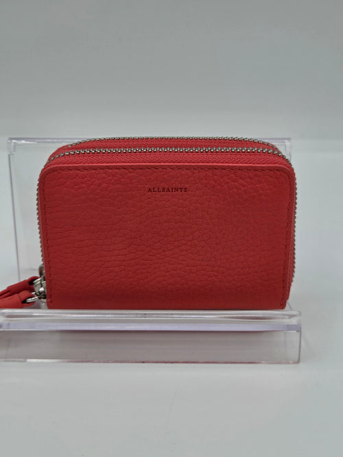 A red textured leather zip-around wallet by Allaints, displayed on a clear acrylic stand against a neutral gray background.