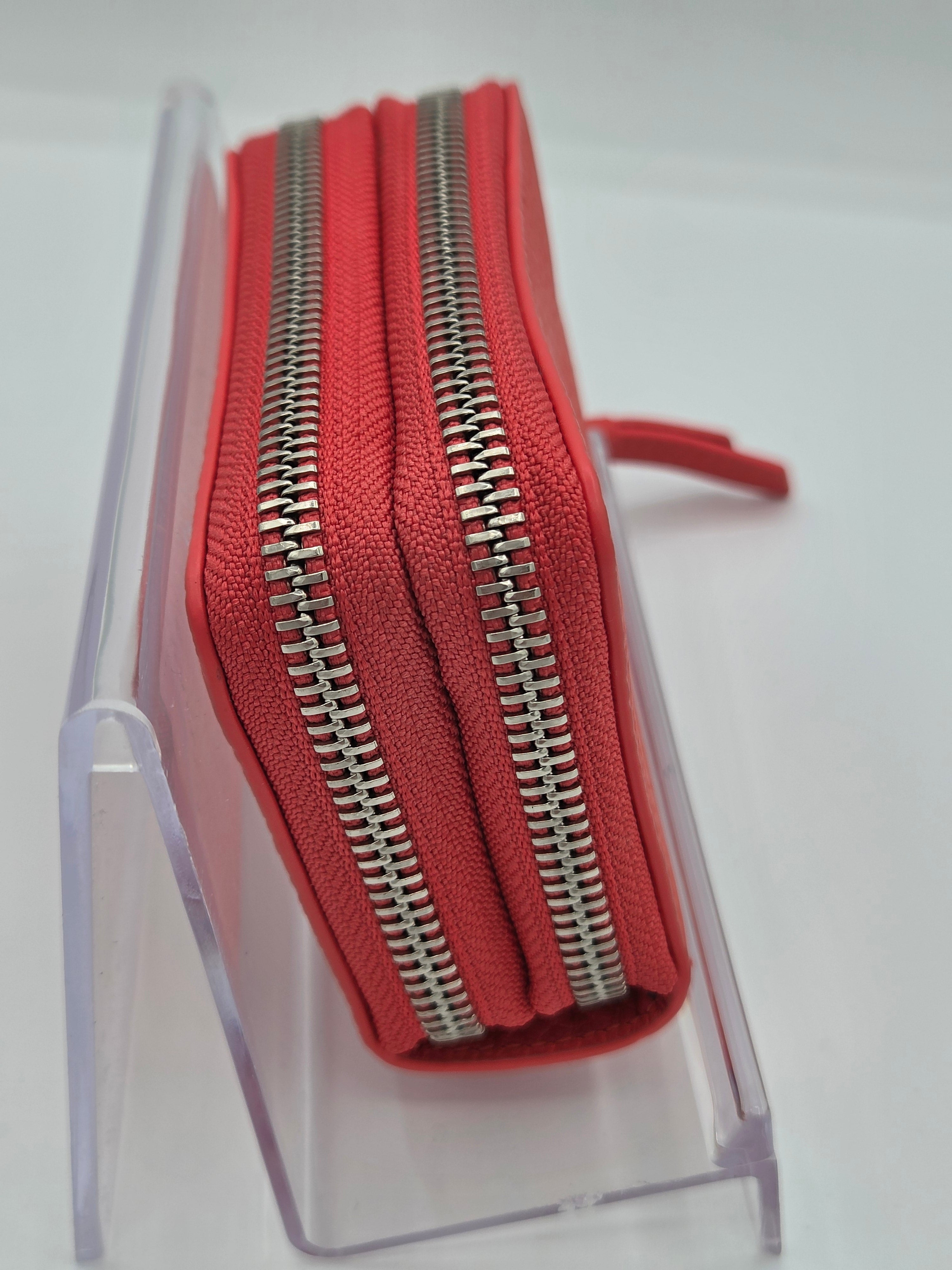A red zip-around wallet with silver metal zippers, displayed in a clear acrylic stand against a white background.