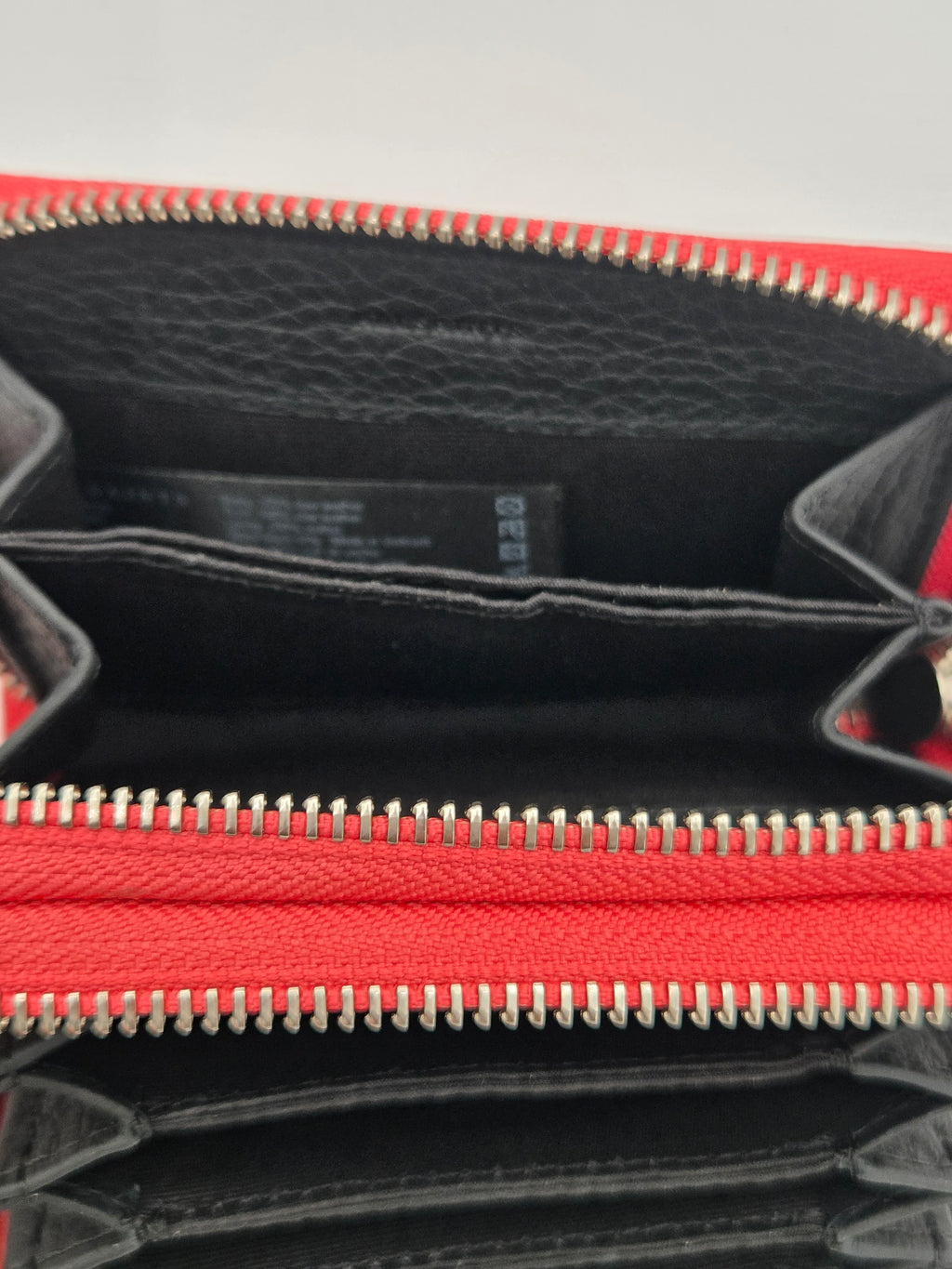 Close-up of a red and black leather zip-around wallet or clutch, showing the interior compartments, black pebbled lining, and silver-toned zipper teeth.