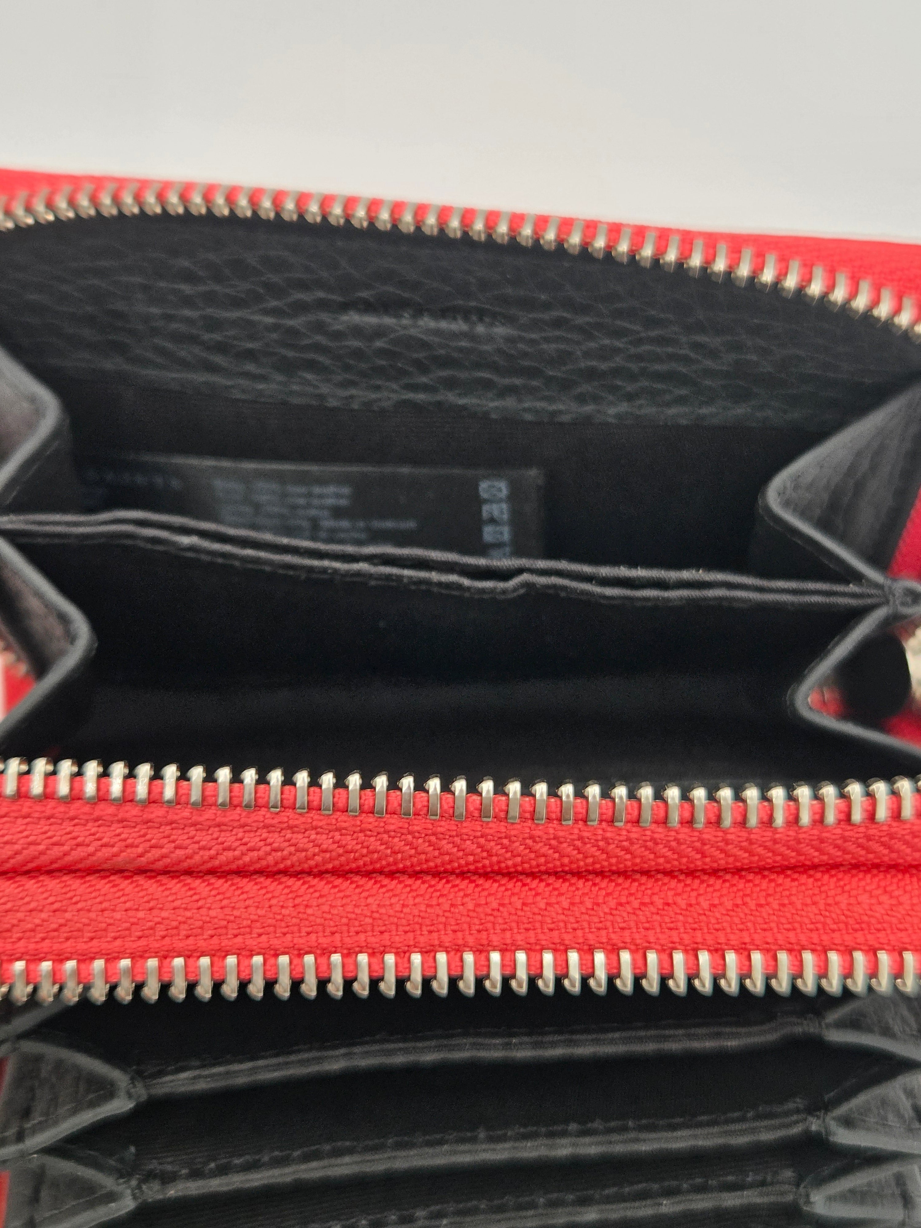 Close-up of a red and black leather zip-around wallet or clutch, showing the interior compartments, black pebbled lining, and silver-toned zipper teeth.