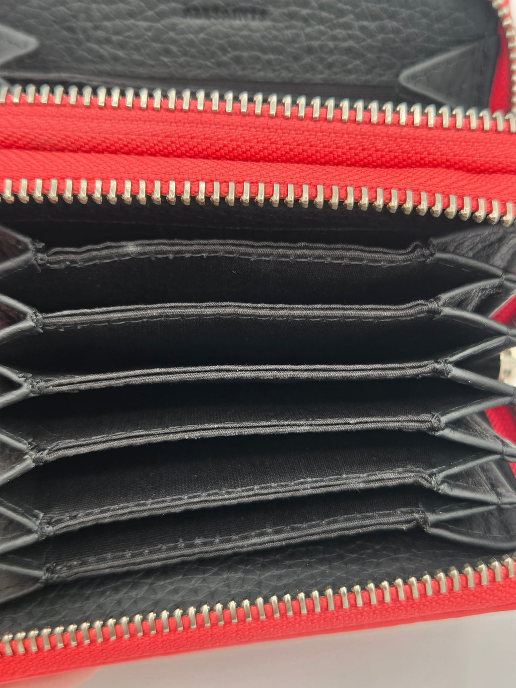 Close-up of an open red and black leather zip-around wallet showing multiple card slots, gold-tone zipper teeth, and interior stitching.
