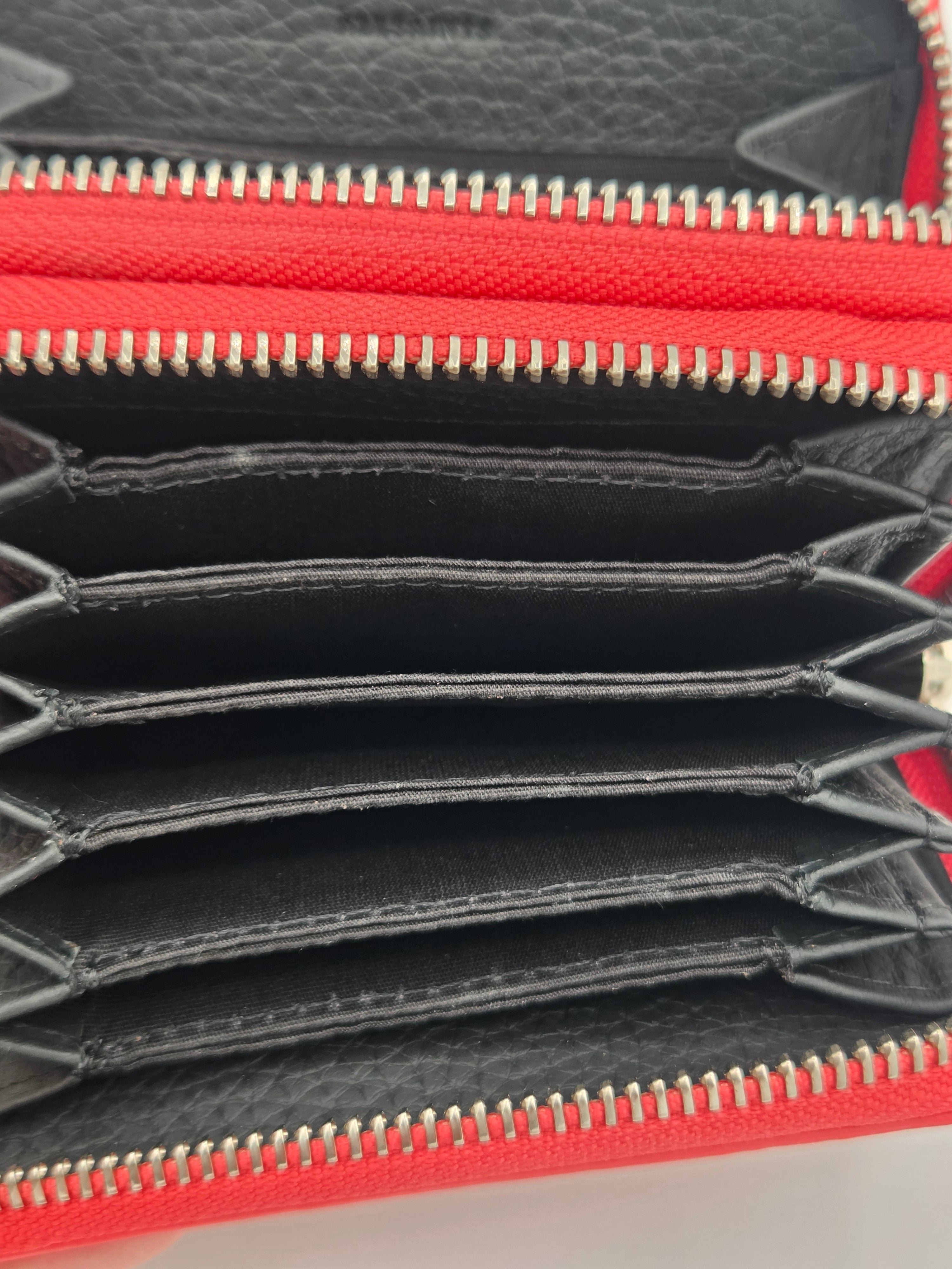 Close-up of an open red and black leather zip-around wallet showing multiple card slots, gold-tone zipper teeth, and interior stitching.