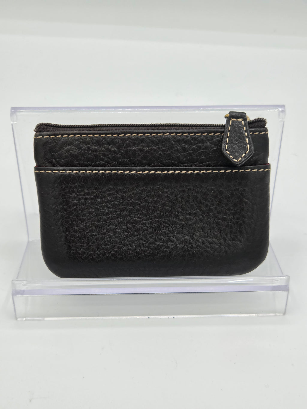 A black pebbled leather zip-around pouch with light tan contrast stitching, displayed inside a clear acrylic stand against a white background.