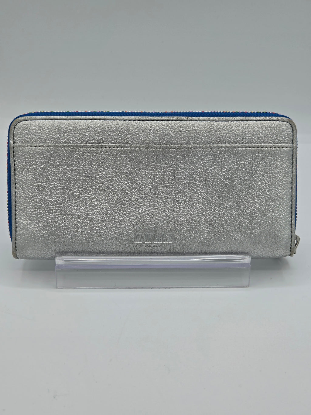 A silver textured leather zip-around wallet with a blue zipper trim, displayed on a clear acrylic stand against a neutral gray background.