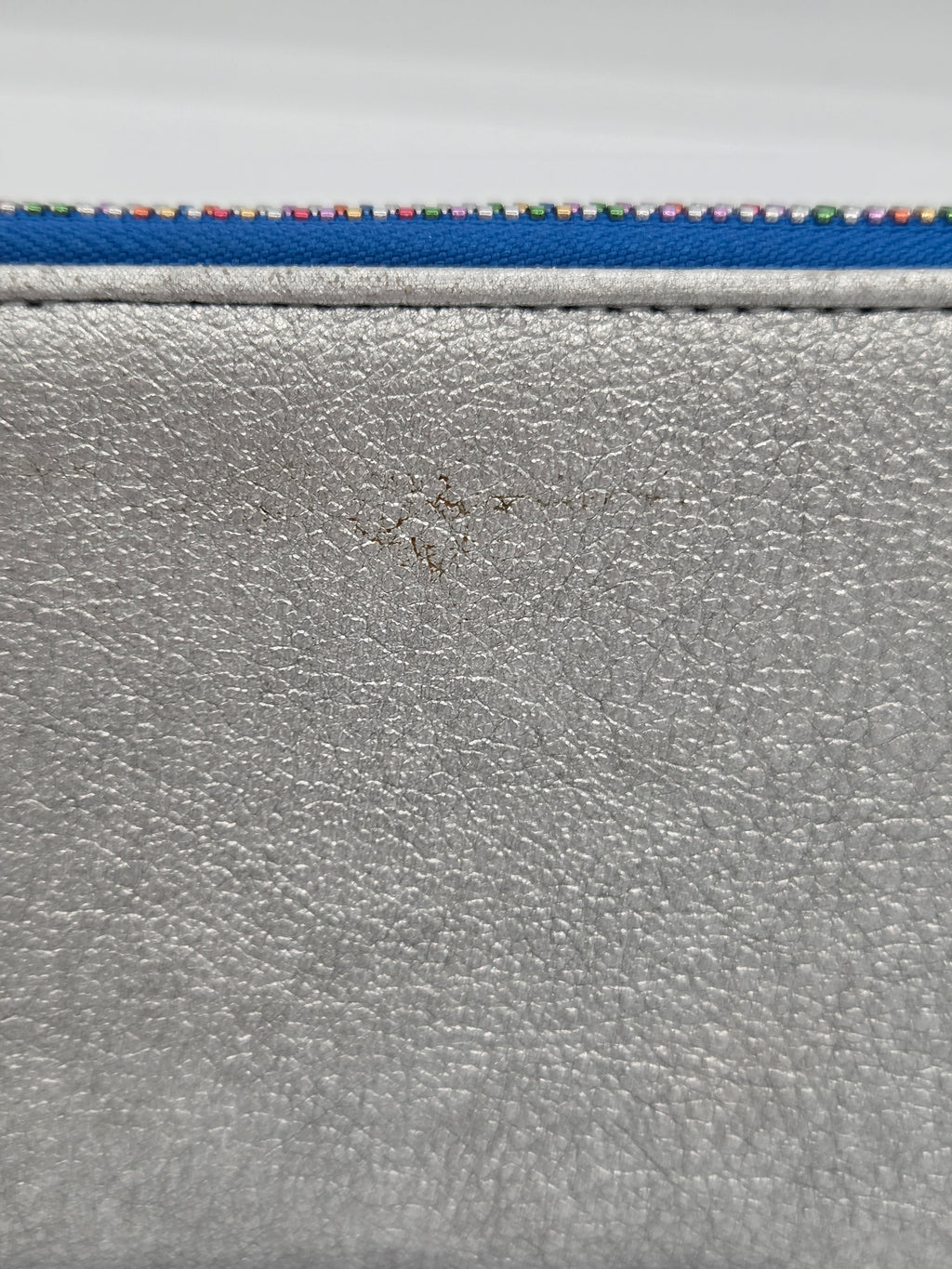 Close-up of a silver textured leather or faux-leather surface with a blue strip and multicolored dotted trim along the top edge.