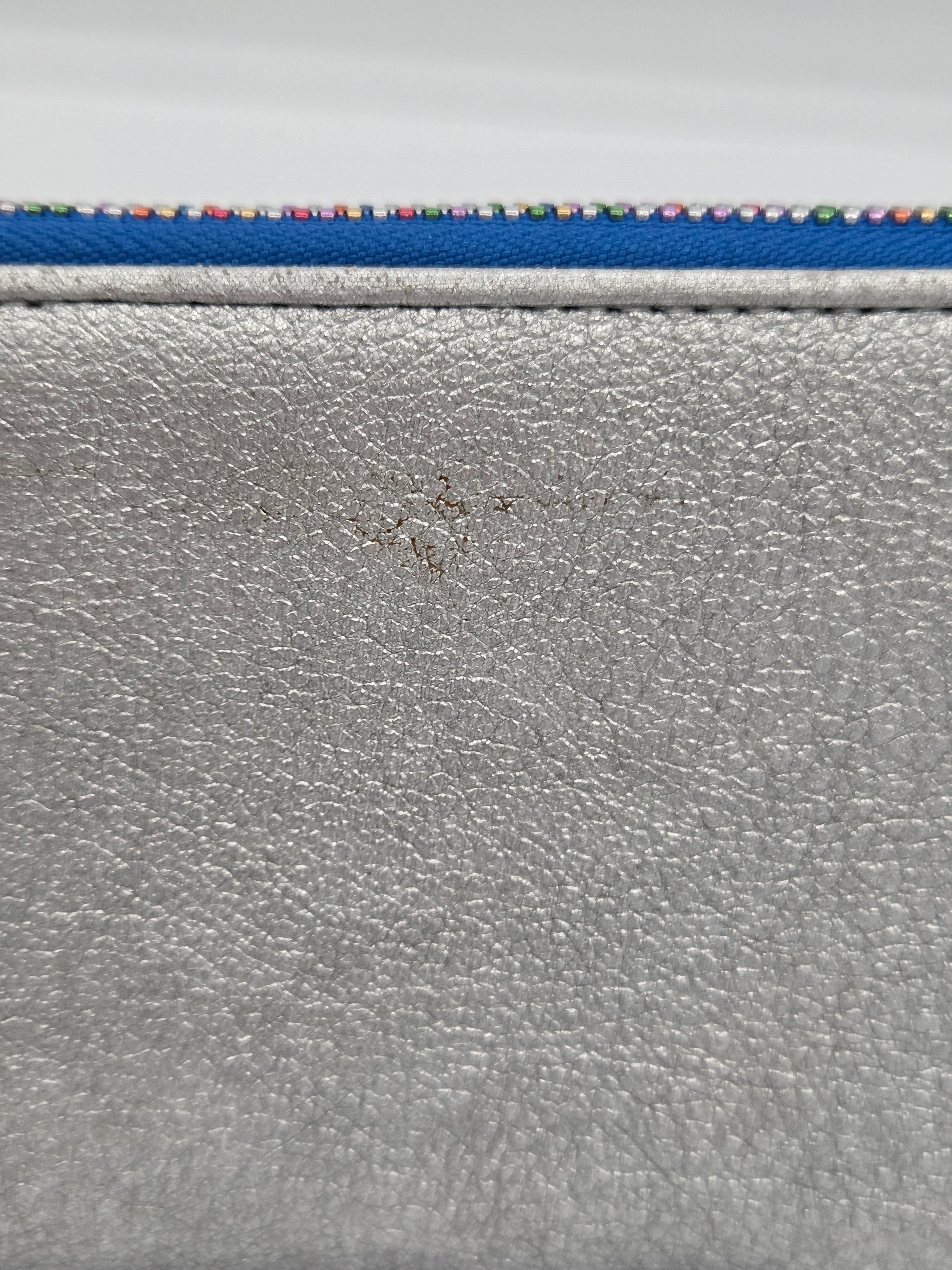 Close-up of a silver textured leather or faux-leather surface with a blue strip and multicolored dotted trim along the top edge.