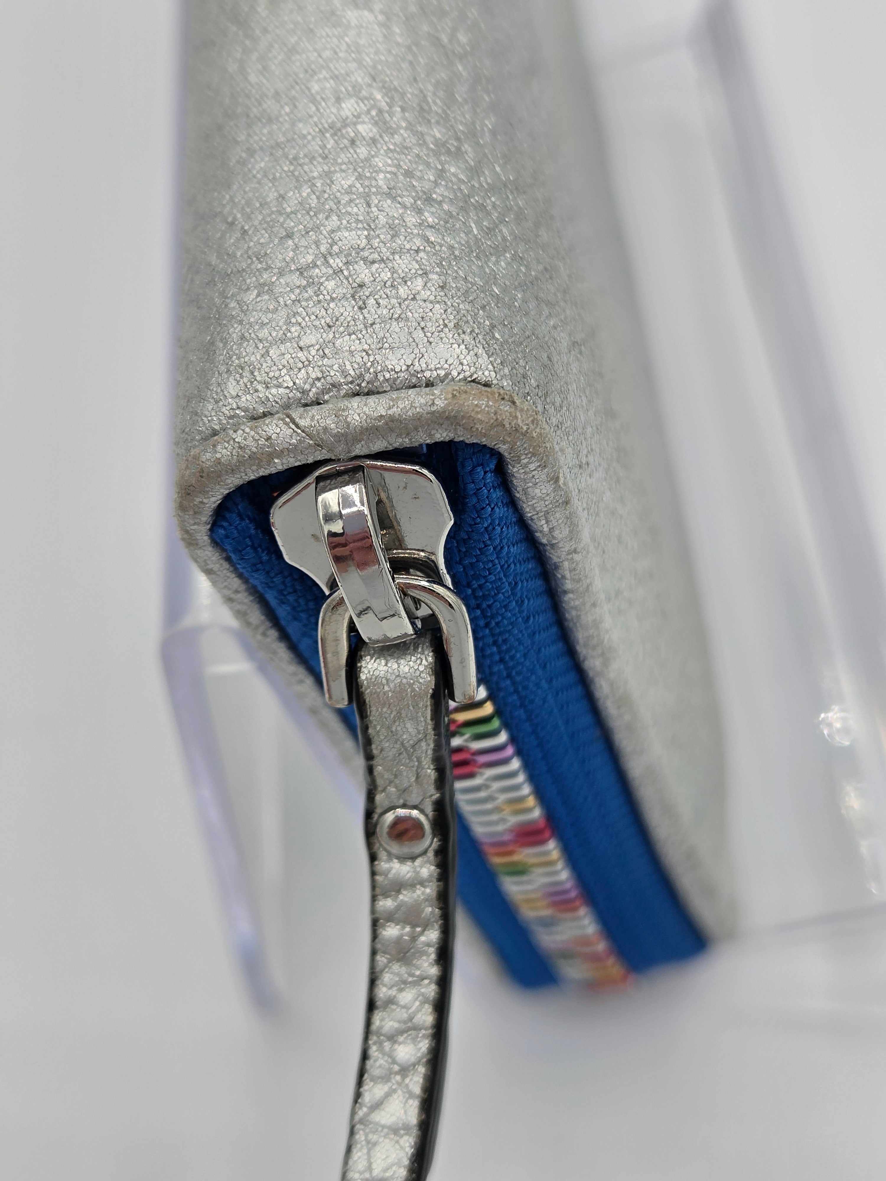 Close-up of a metallic silver zippered pouch with a blue zipper track and a silver wristlet strap, shown on a white background.