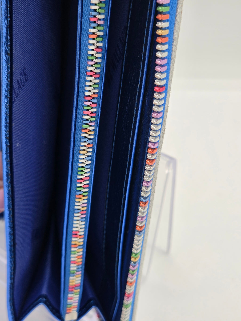 Close-up of a blue fabric zippered pouch or organizer with colorful embroidered or bead-like detailing along the zipper edges, shown against a white background.