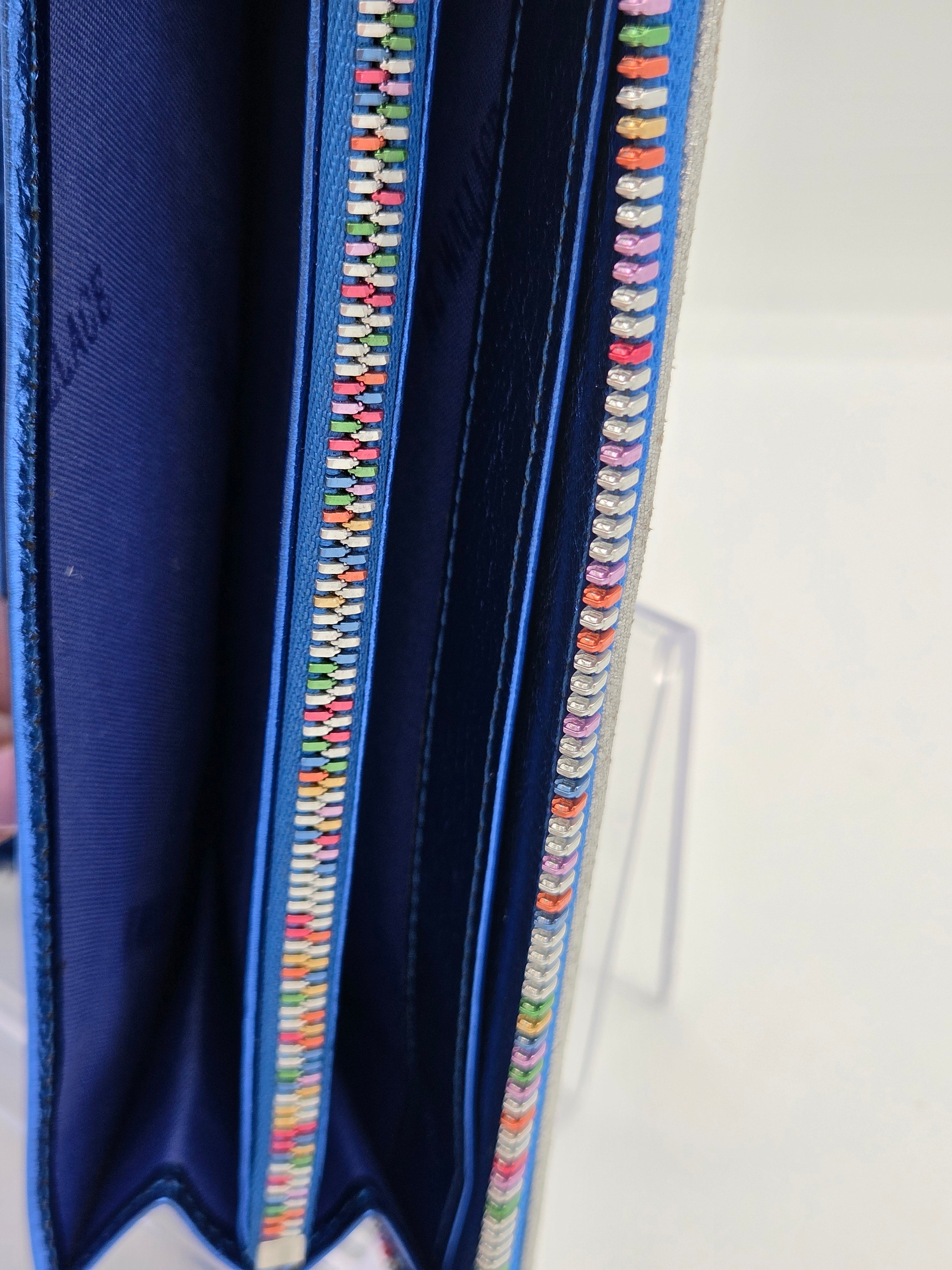 Close-up of a blue fabric zippered pouch or organizer with colorful embroidered or bead-like detailing along the zipper edges, shown against a white background.