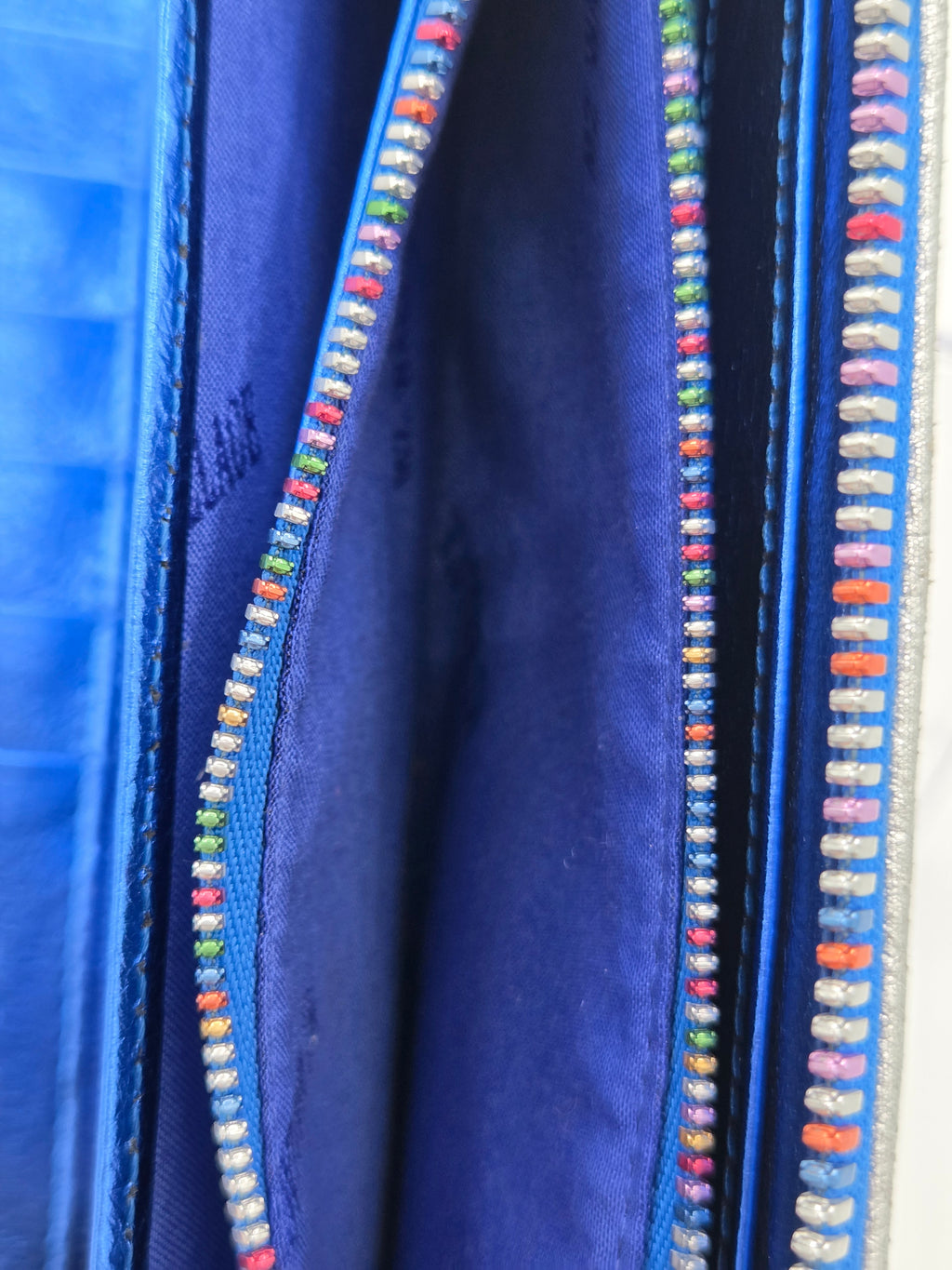 Close-up of a blue fabric item, likely a wallet or organizer, showing a blue interior lined with colorful embroidered or beaded trim along the edges.