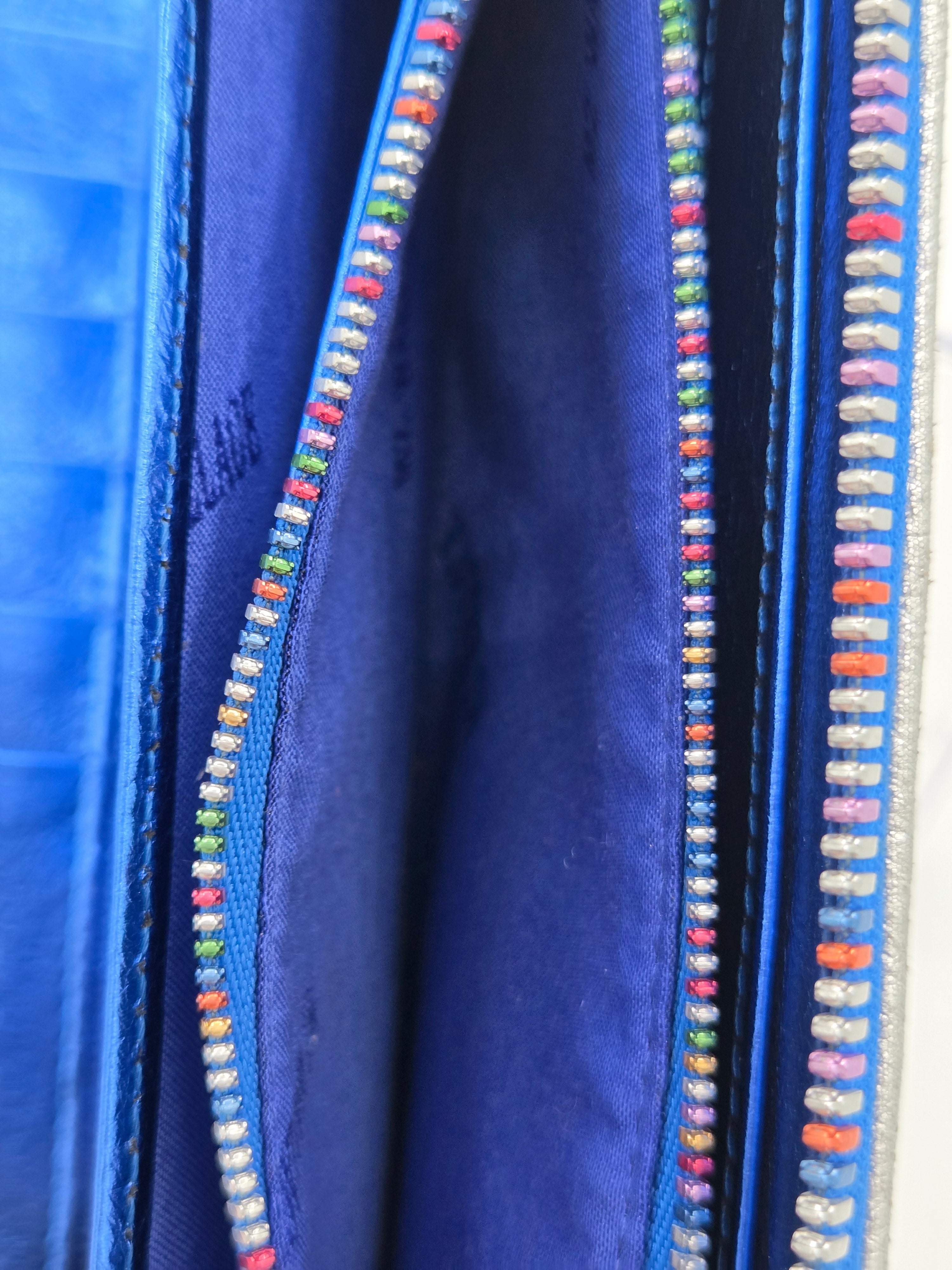 Close-up of a blue fabric item, likely a wallet or organizer, showing a blue interior lined with colorful embroidered or beaded trim along the edges.