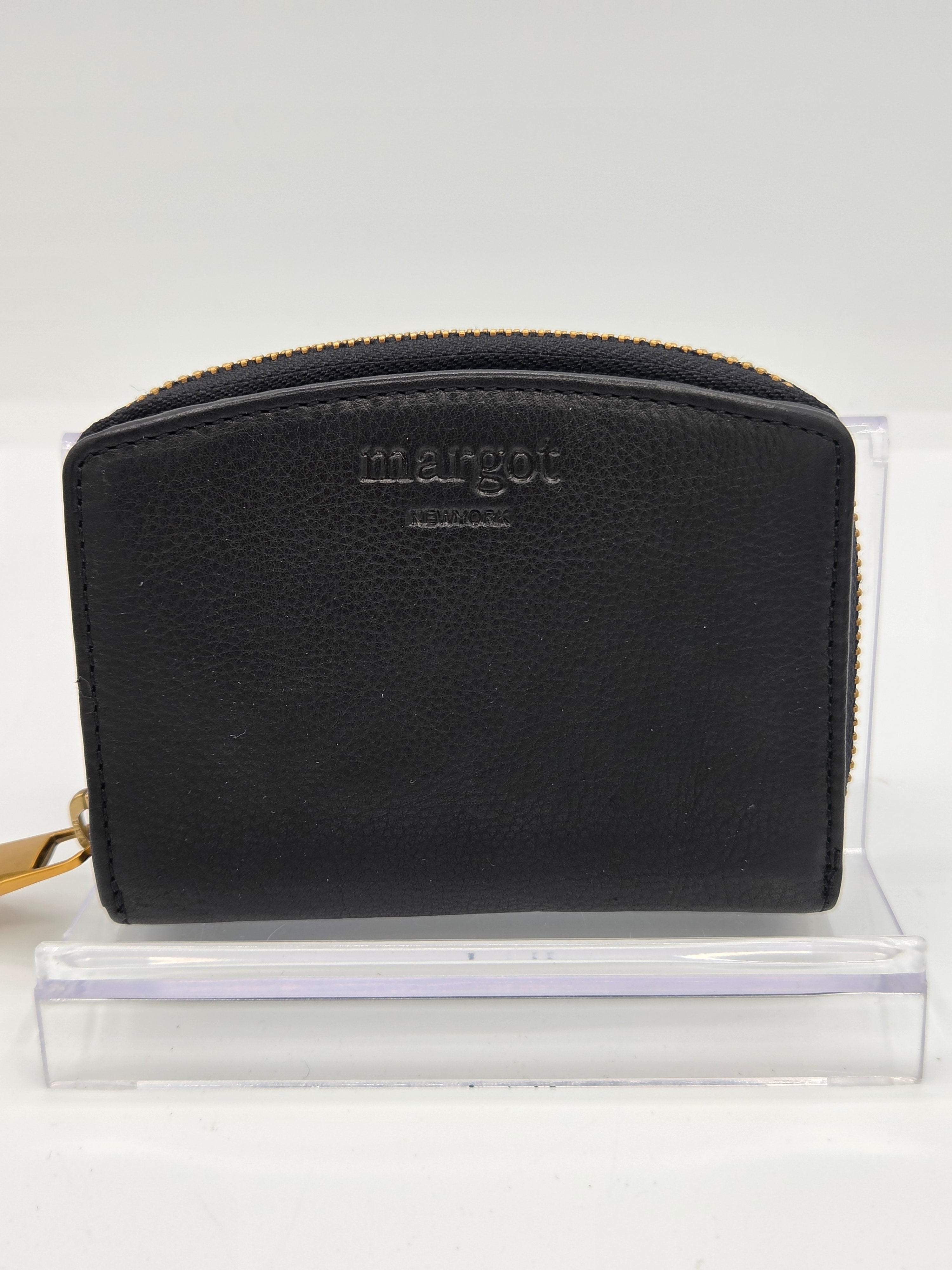 A black pebbled leather zip-around wallet by Margot, displayed on a clear acrylic stand against a white background.