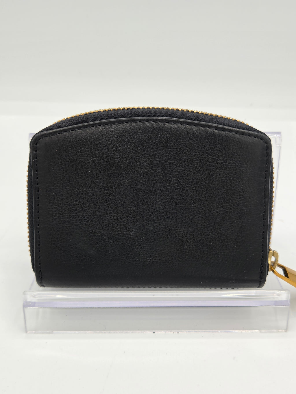 A black pebbled leather zip-around wallet with gold-tone hardware, displayed on a clear acrylic stand against a white background.