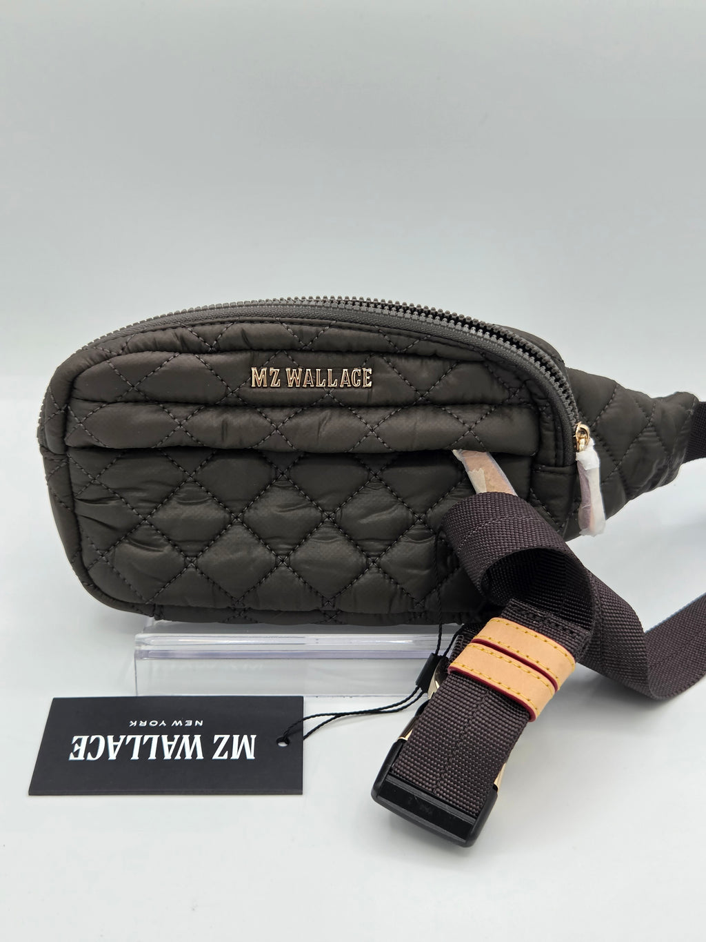 A dark brown quilted MZ Wallace fanny pack with a matching adjustable strap and a black brand tag, displayed on a light gray background.