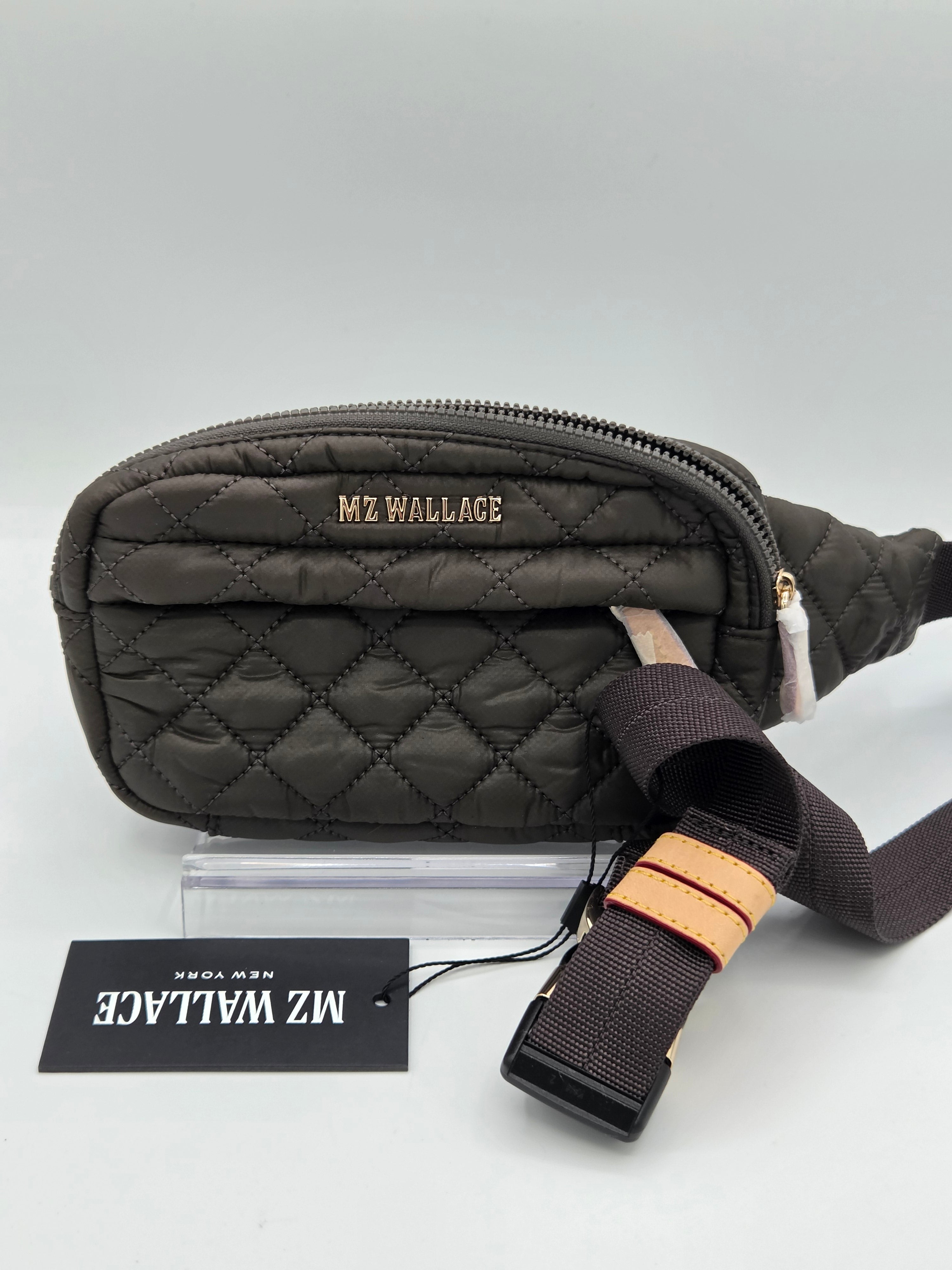 A dark brown quilted MZ Wallace fanny pack with a matching adjustable strap and a black brand tag, displayed on a light gray background.