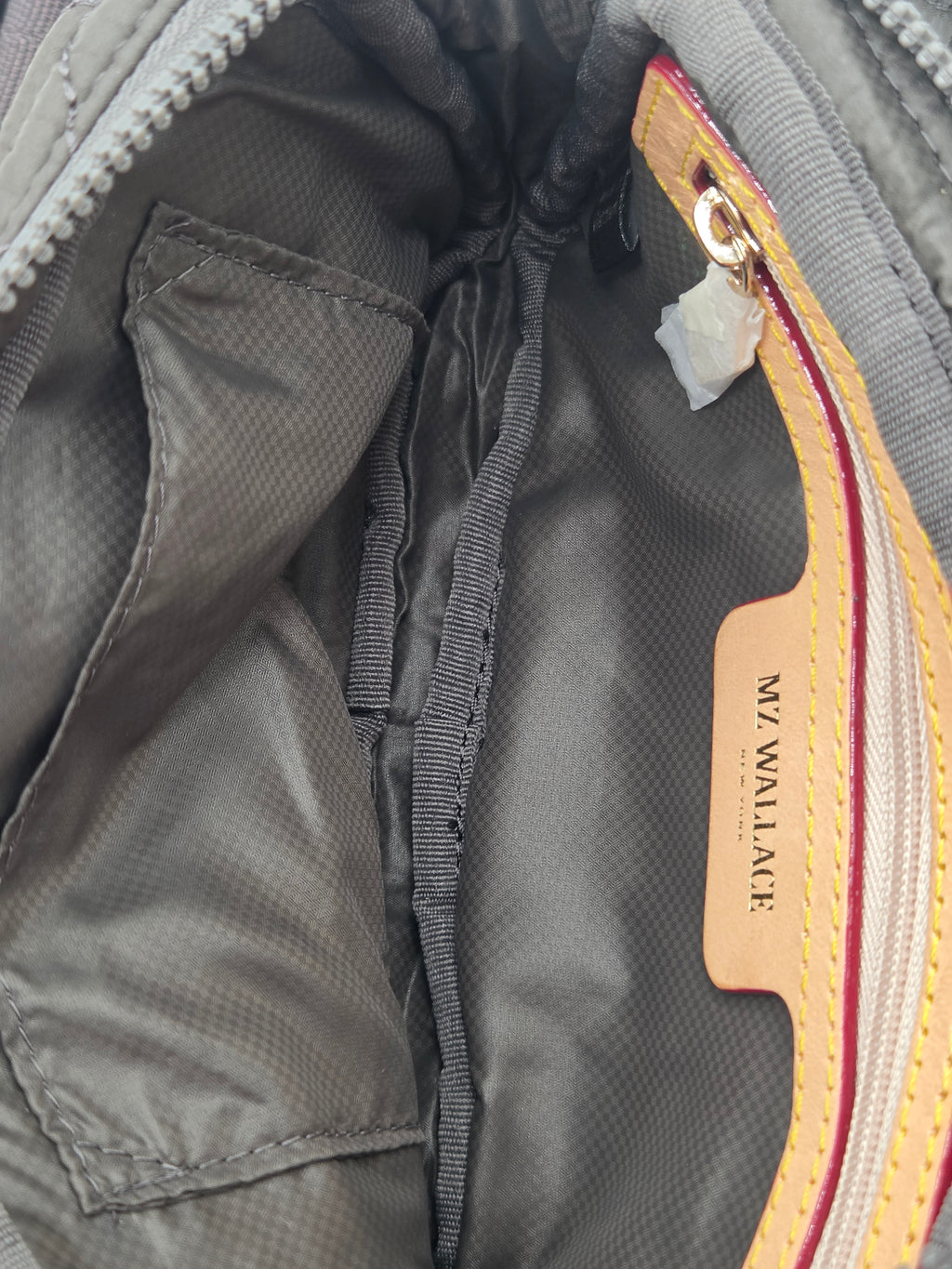 Close-up of the interior of a gray nylon bag, showing a zippered pocket with a tan leather brand tab that reads 'N.Y.