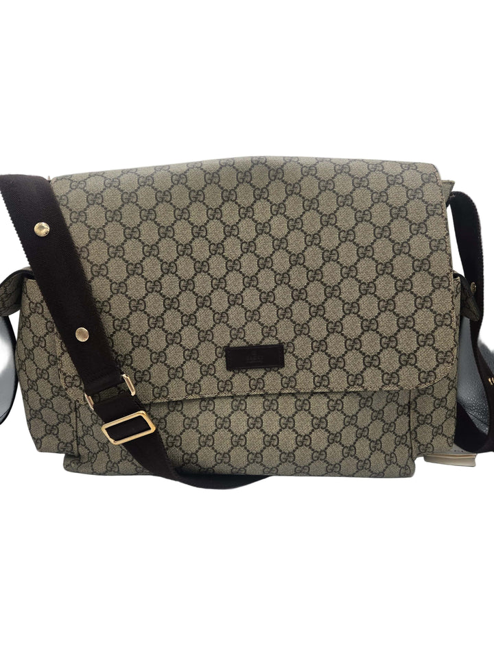 A vintage-style shoulder bag featuring the classic beige and brown GG monogram canvas, a dark brown leather strap with gold-tone hardware, and a small black leather brand plaque on the front flap.