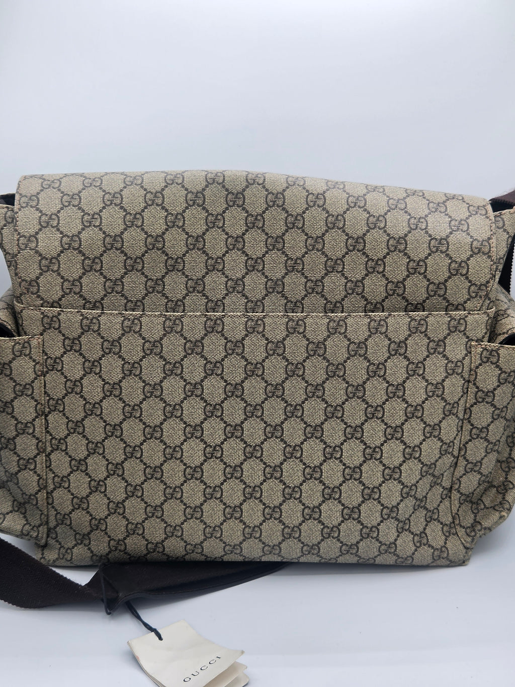 A Gucci shoulder bag in the classic GG Supreme canvas, featuring a beige and brown repeating monogram pattern, with a black strap and a Gucci dust bag visible below on a white background.