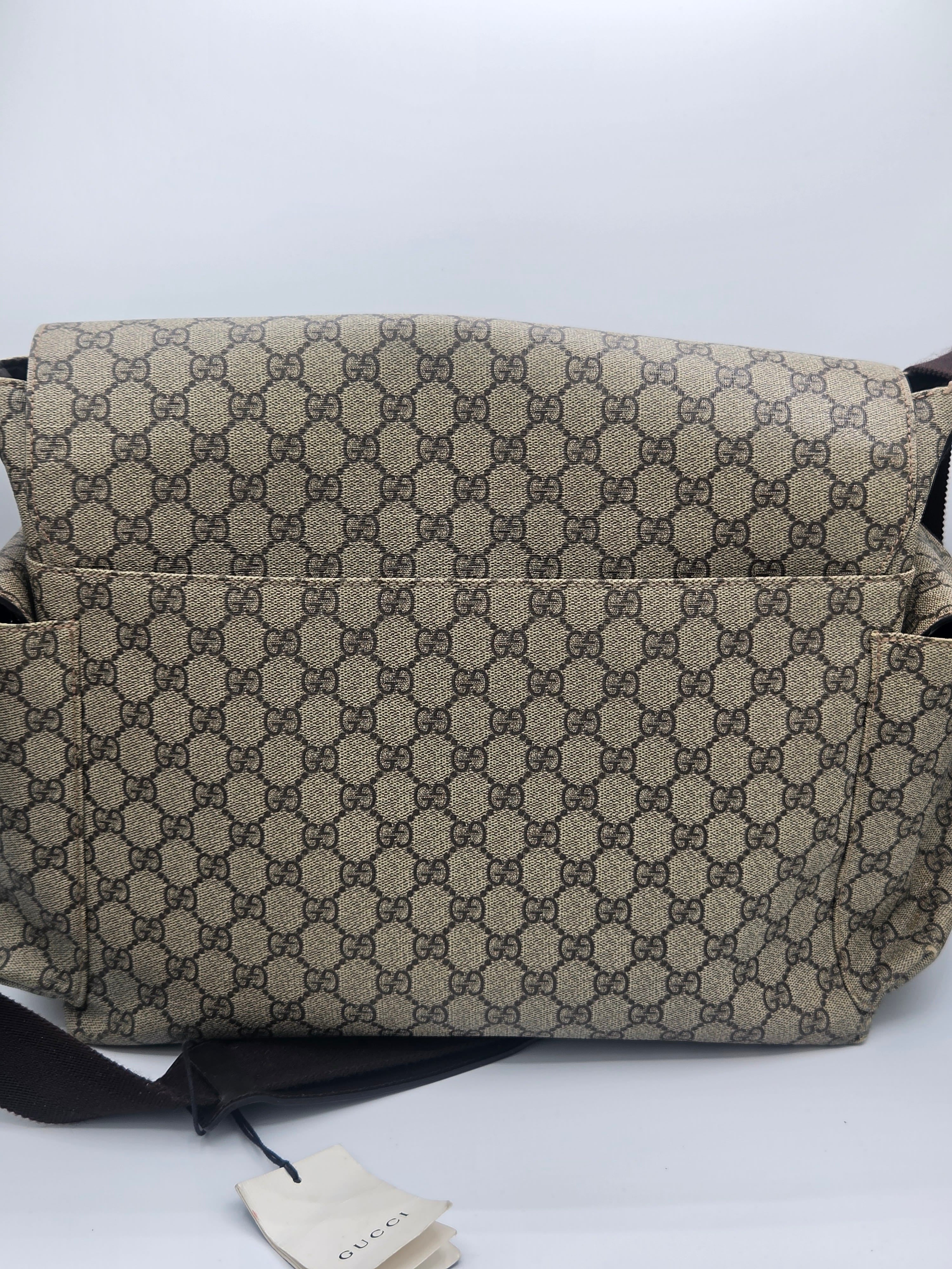 A Gucci shoulder bag in the classic GG Supreme canvas, featuring a beige and brown repeating monogram pattern, with a black strap and a Gucci dust bag visible below on a white background.