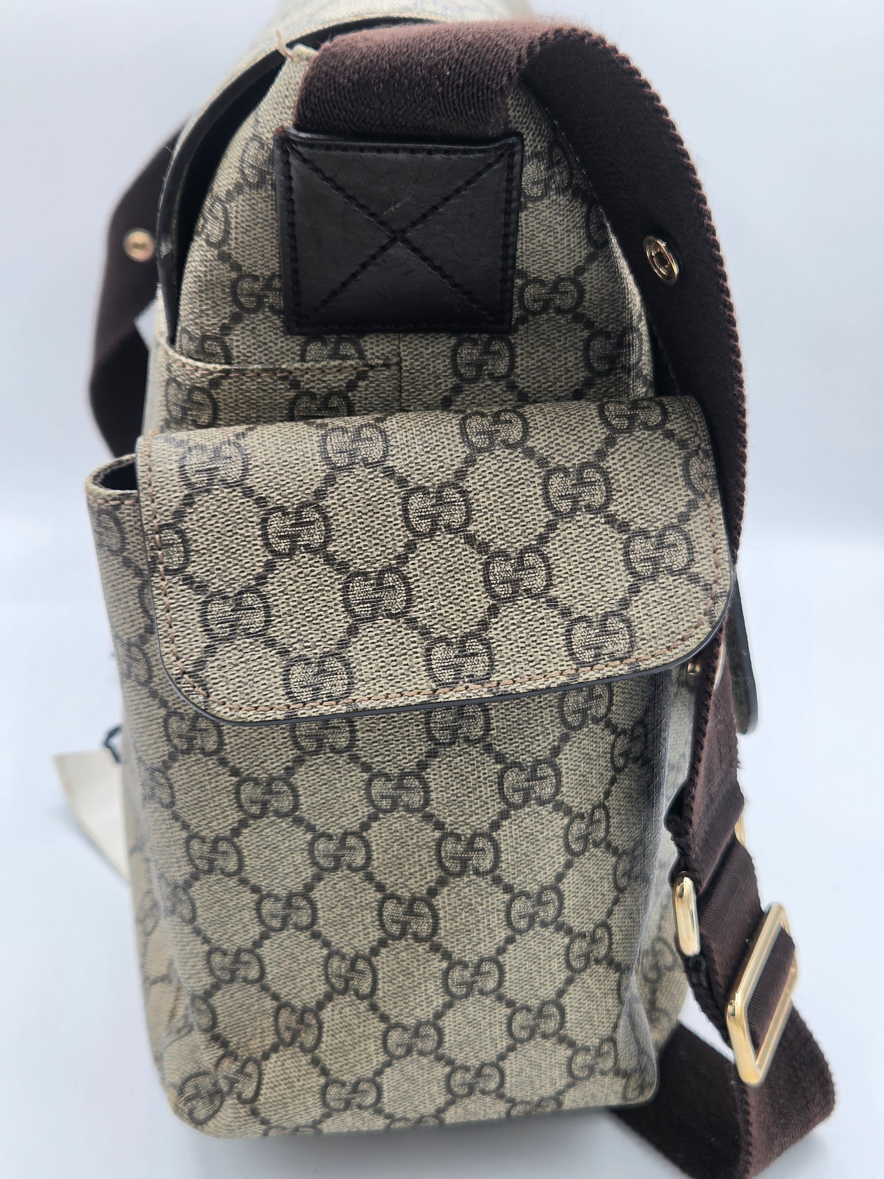 A Gucci shoulder bag in beige and brown GG Supreme canvas with dark brown leather trim and a gold-tone buckle, shown against a light gray background.