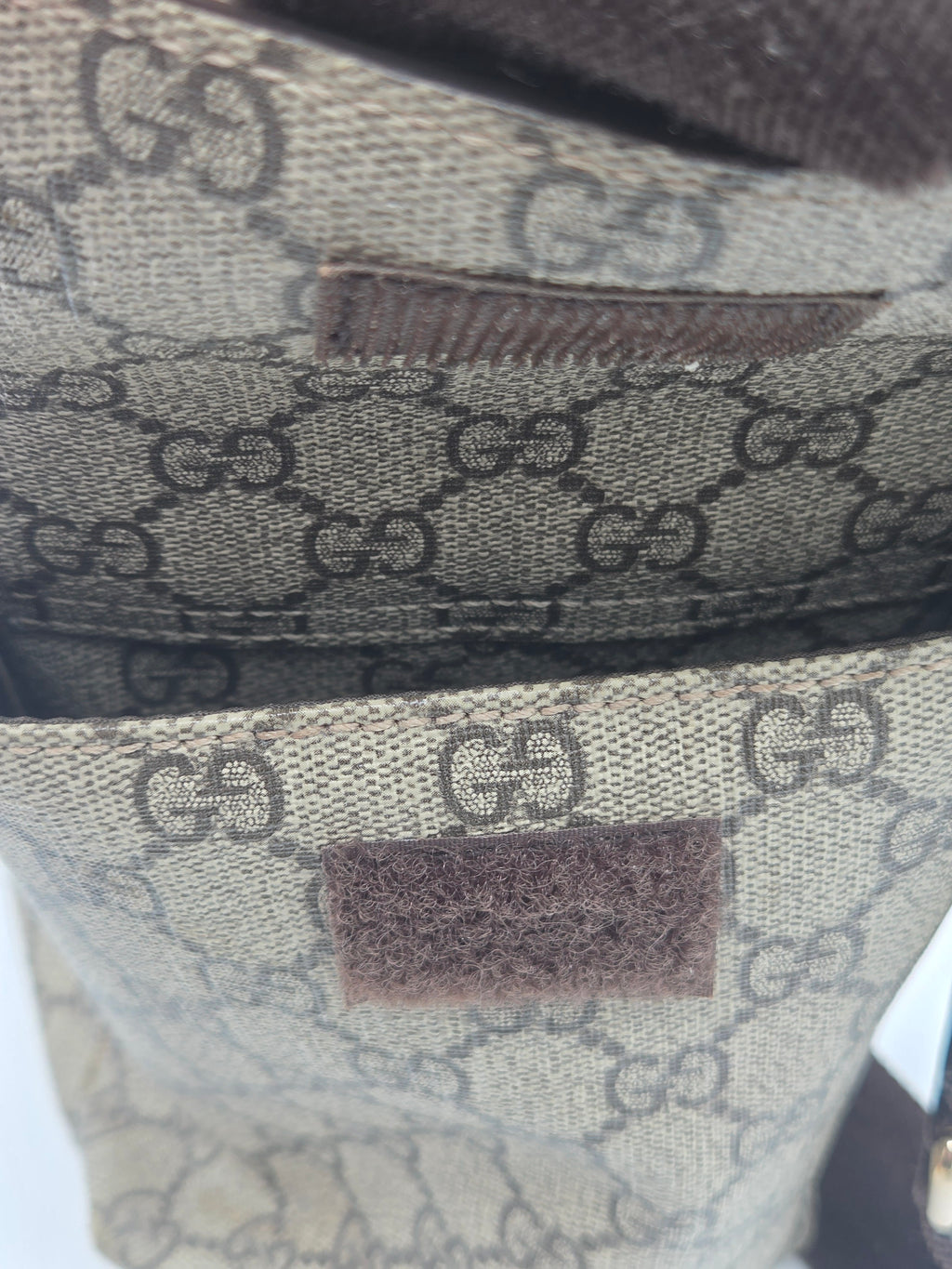 Close-up of a beige and brown monogram canvas bag with a dark brown leather patch and a brown hook-and-loop fastener.