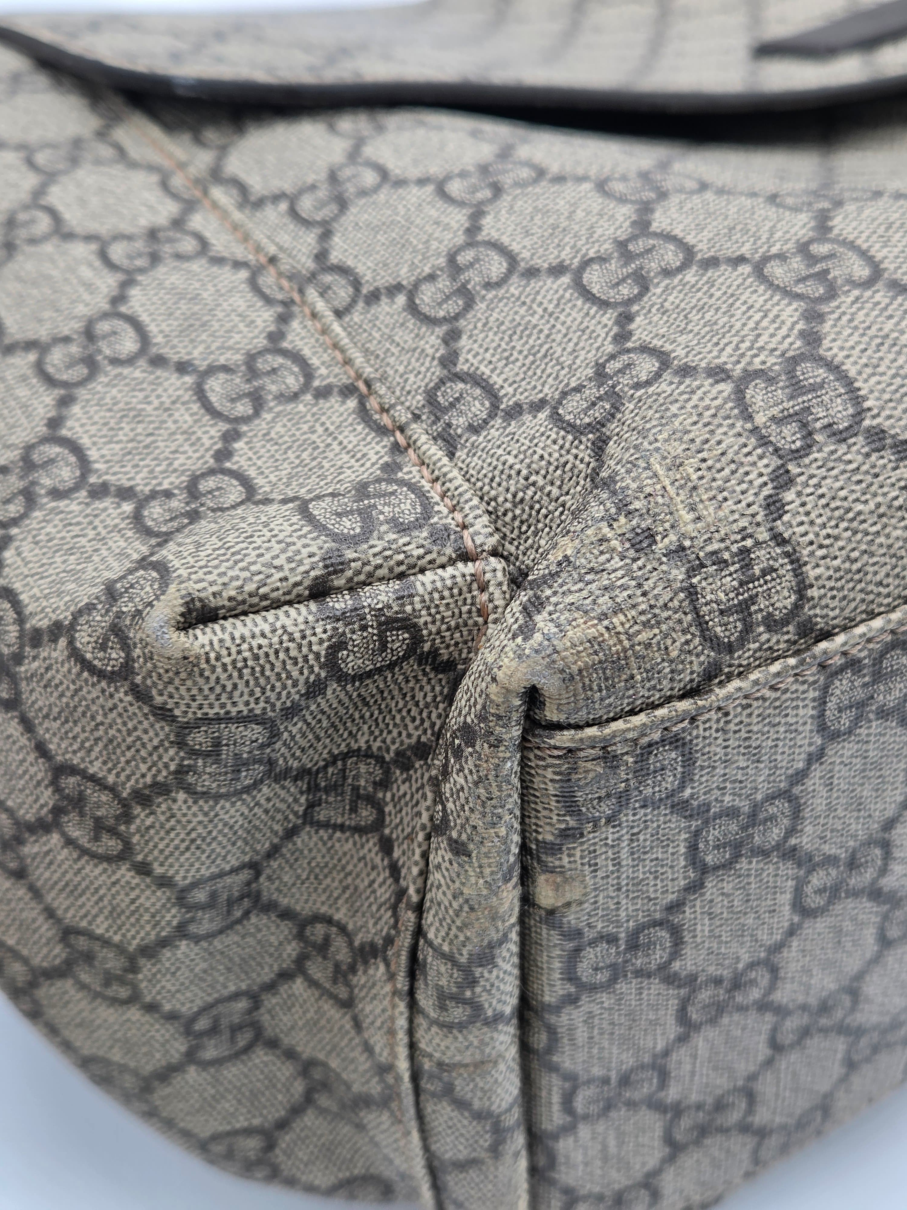Close-up of a beige and brown GG Supreme canvas bag corner showing the classic interlocking G pattern and stitched construction details.