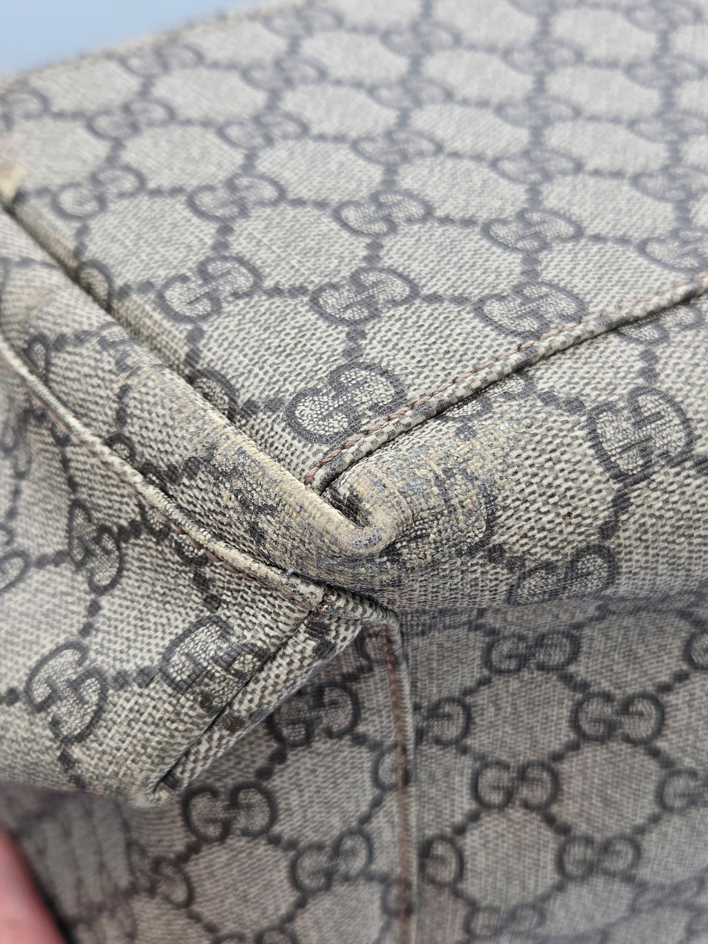Close-up of a beige and brown monogram canvas material with a visible fold and stitching detail.