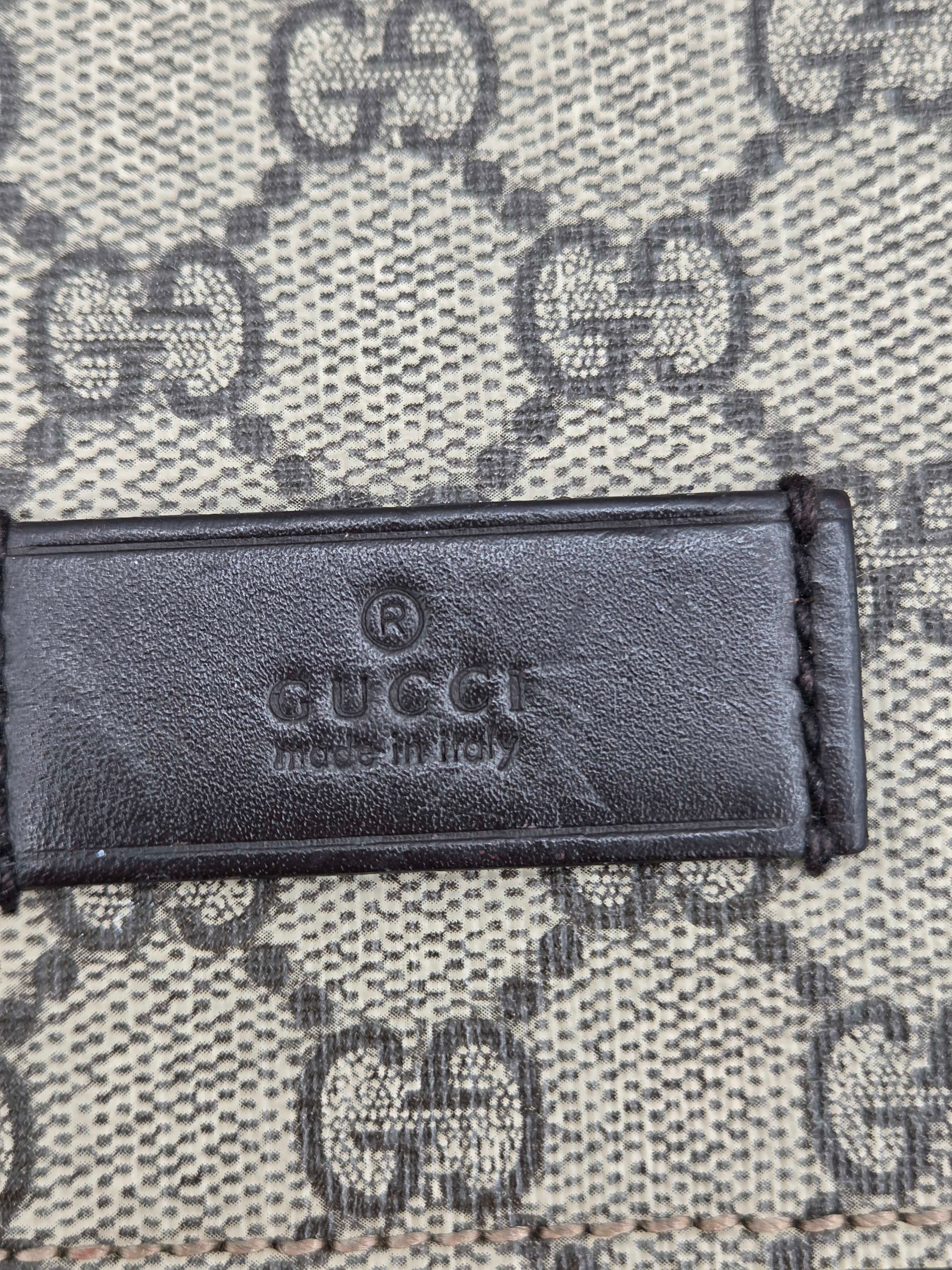Close-up of a Gucci leather label embossed with 'GUCCI made in Italy' on a beige and gray GG Supreme canvas background.