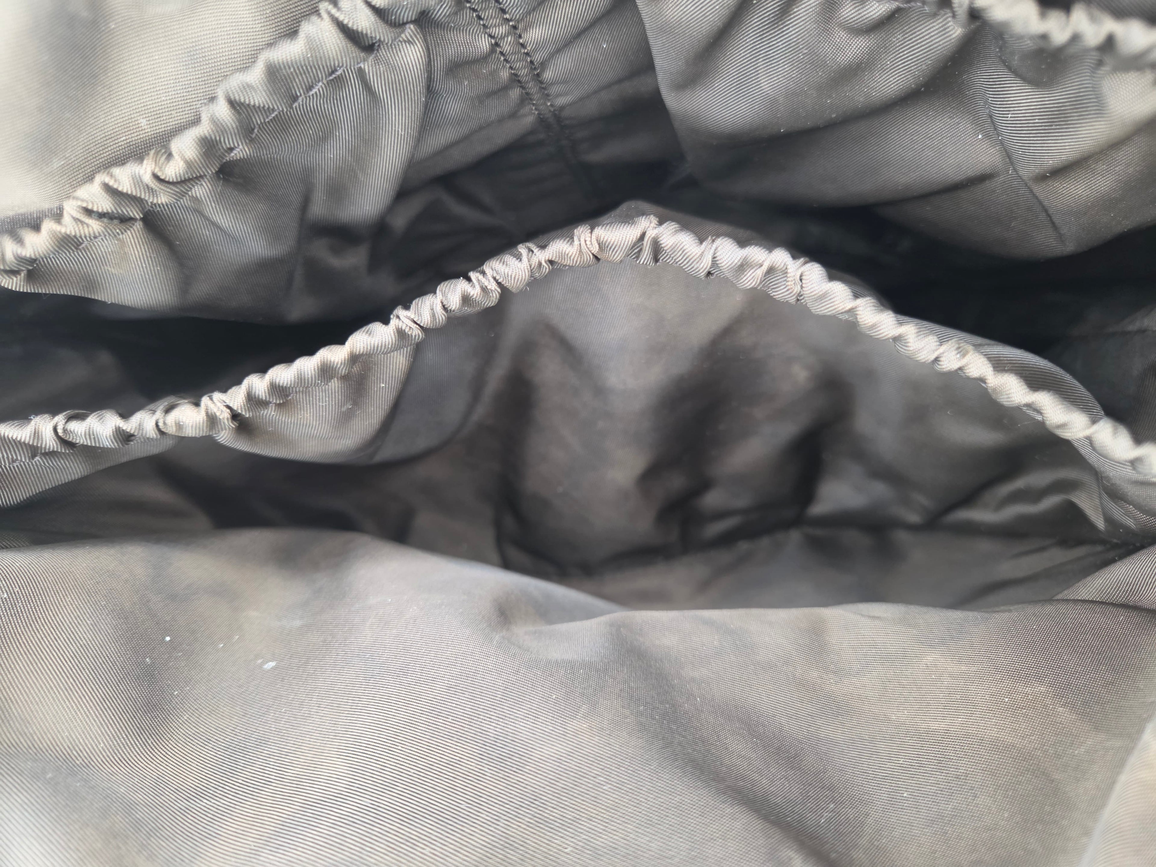 Close-up of a dark gray fabric pouch or pocket showing the interior lining and elasticized gathered edge.