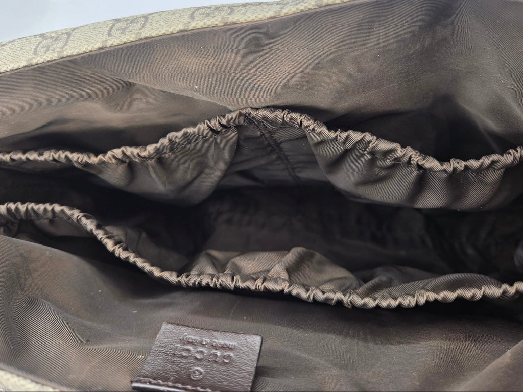 Close-up of the interior lining of a Gucci bag, showing dark brown satin-like fabric with elasticized compartments and a small Gucci leather tag near the bottom.