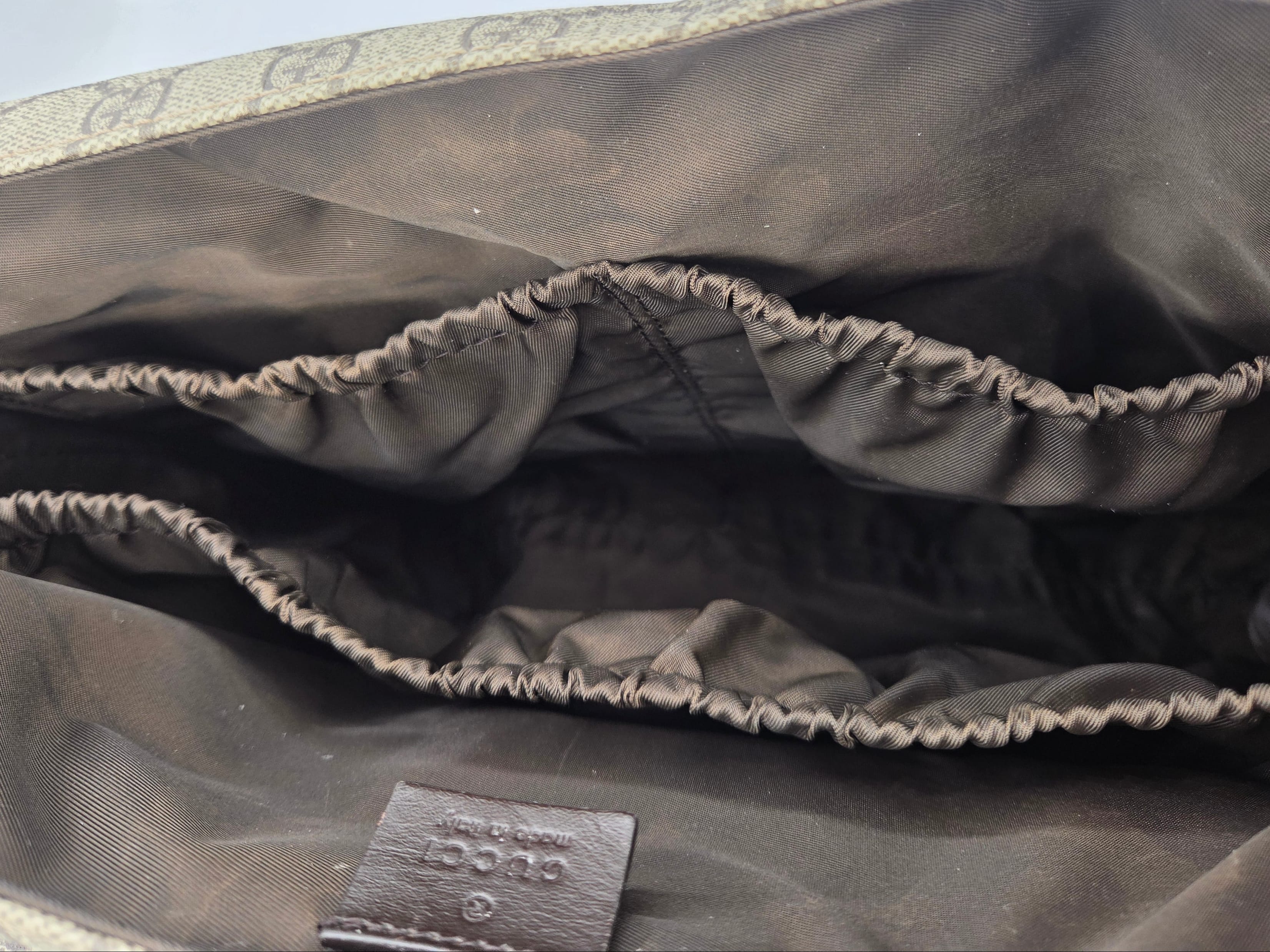 Close-up of the interior lining of a Gucci bag, showing dark brown satin-like fabric with elasticized compartments and a small Gucci leather tag near the bottom.