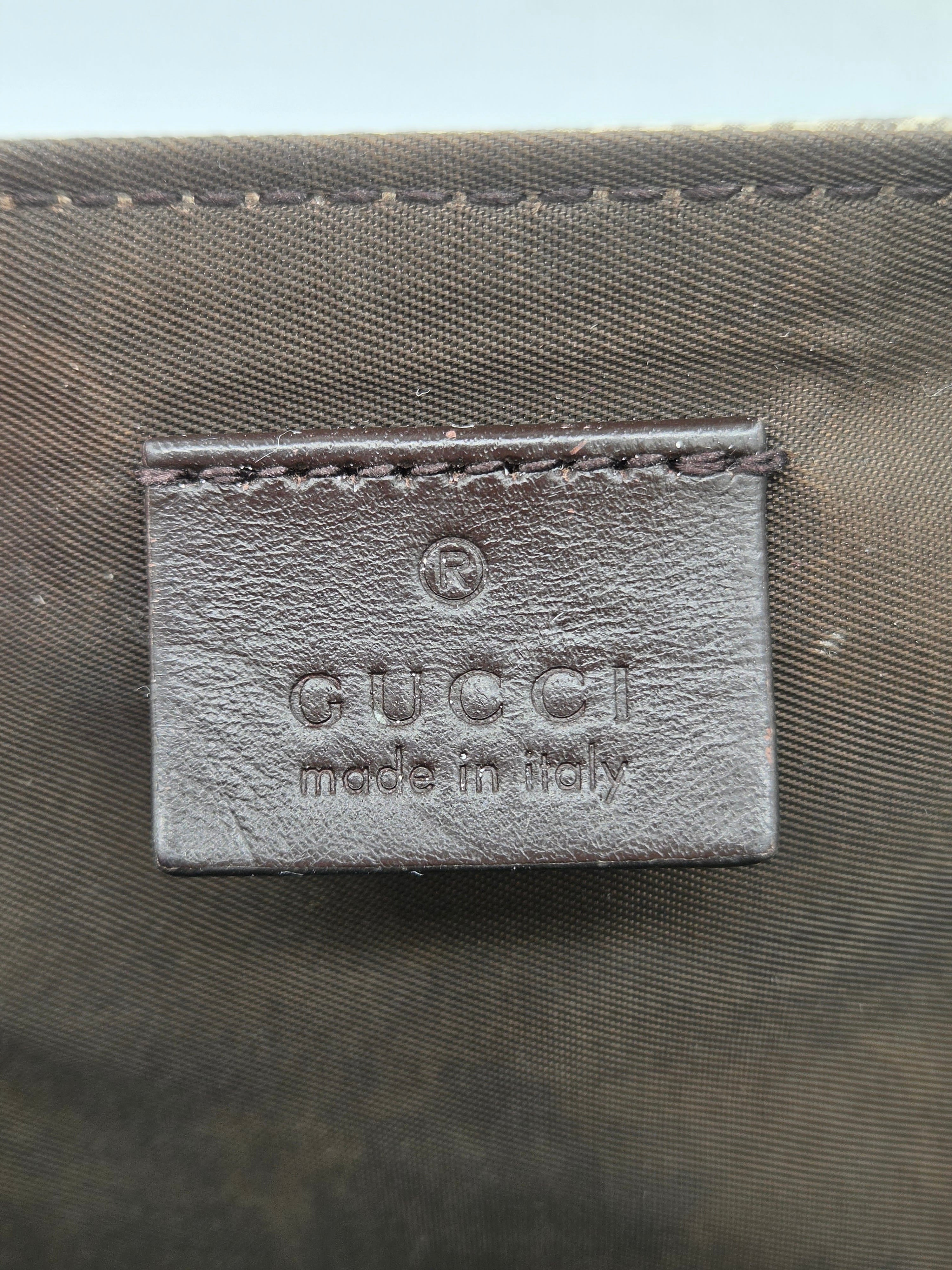 Close-up of a Gucci leather label embossed with 'GUCCI made in Italy' on a dark olive green woven fabric background.