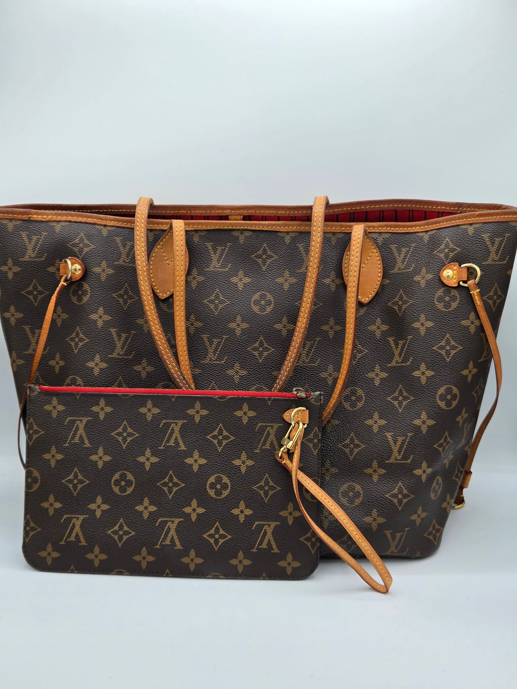 A Louis Vuitton monogram tote bag in dark brown coated canvas with tan leather handles and trim, shown with a matching zippered pouch in front on a light gray studio background.