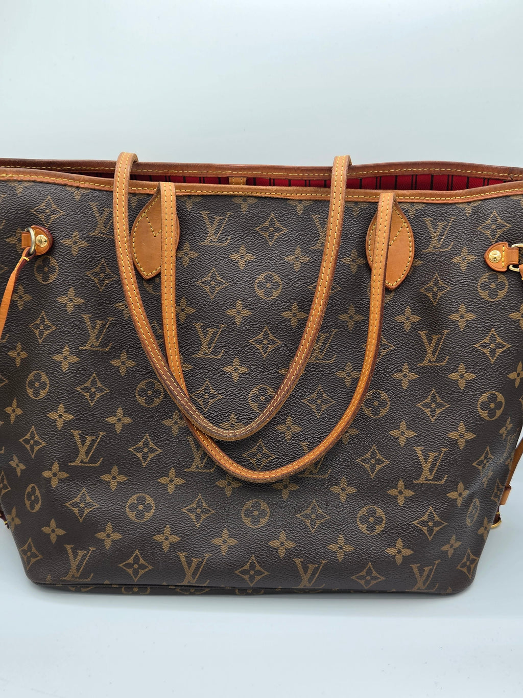A Louis Vuitton monogram canvas tote bag with tan leather handles and trim, shown against a plain light gray background.