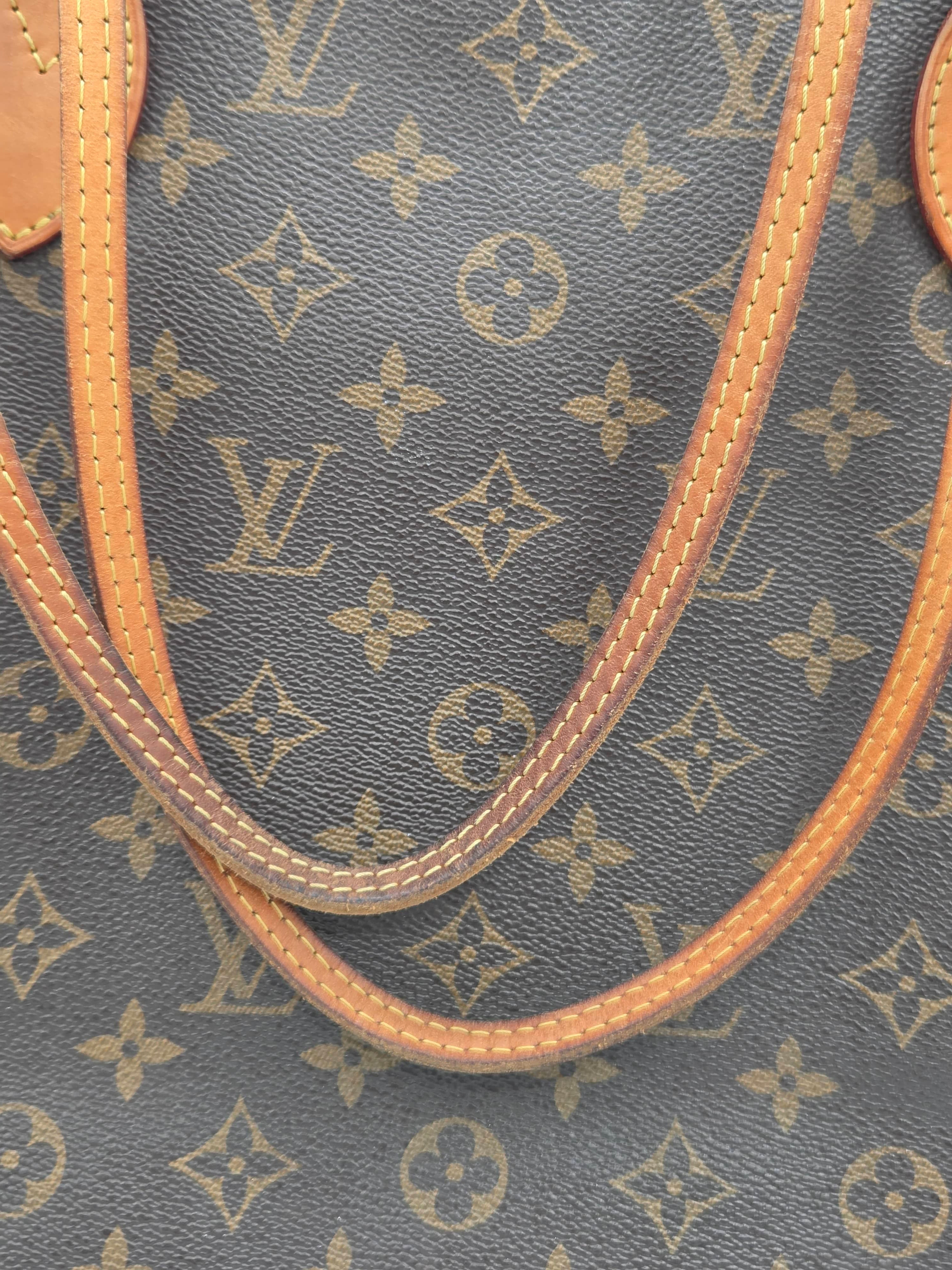 Close-up of a Louis Vuitton monogram canvas bag with tan leather handles and trim, showing the repeating LV logo pattern.