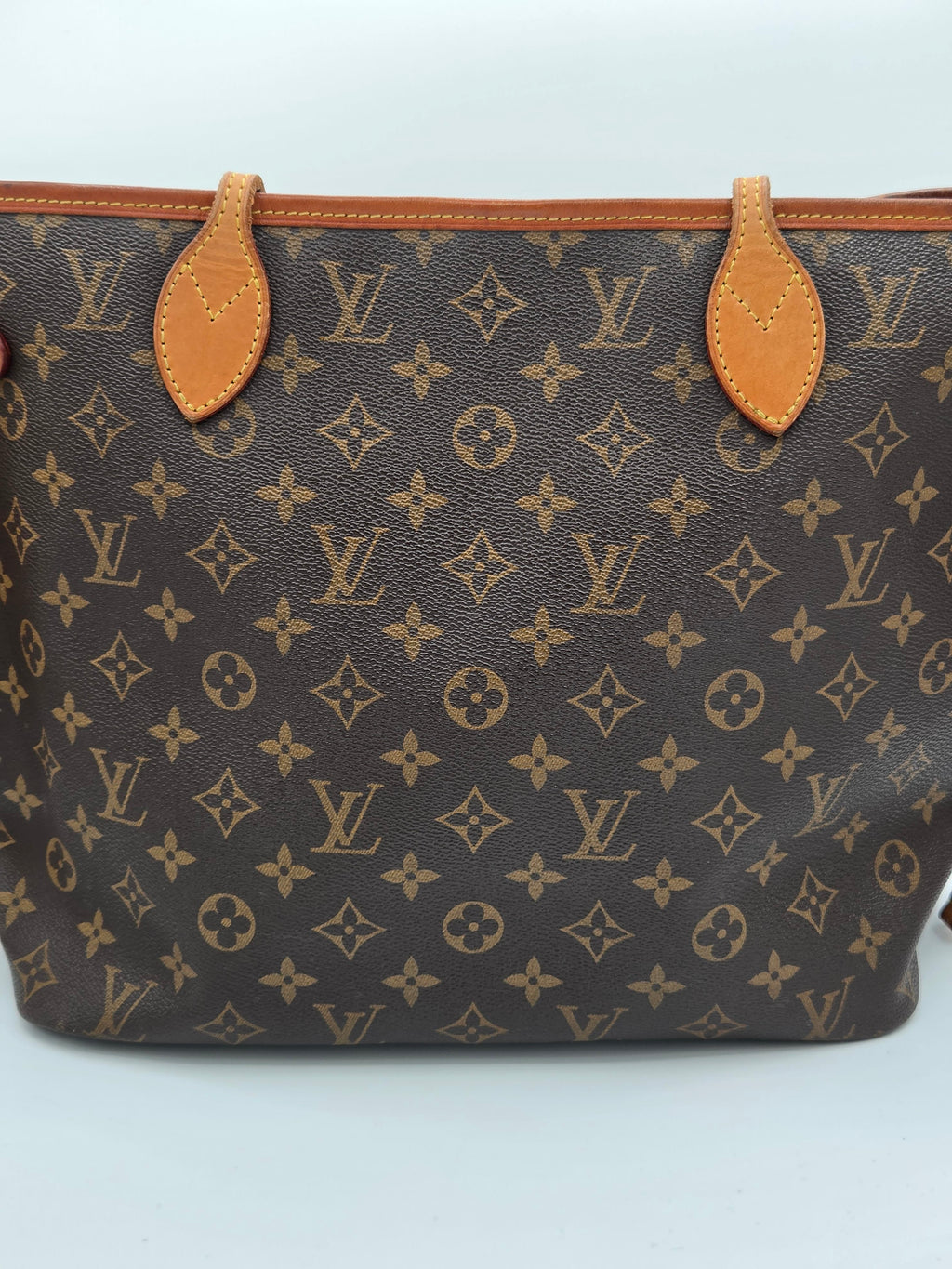 Louis Vuitton monogram canvas tote bag in dark brown with tan leather trim and handle attachments, photographed against a light gray background.