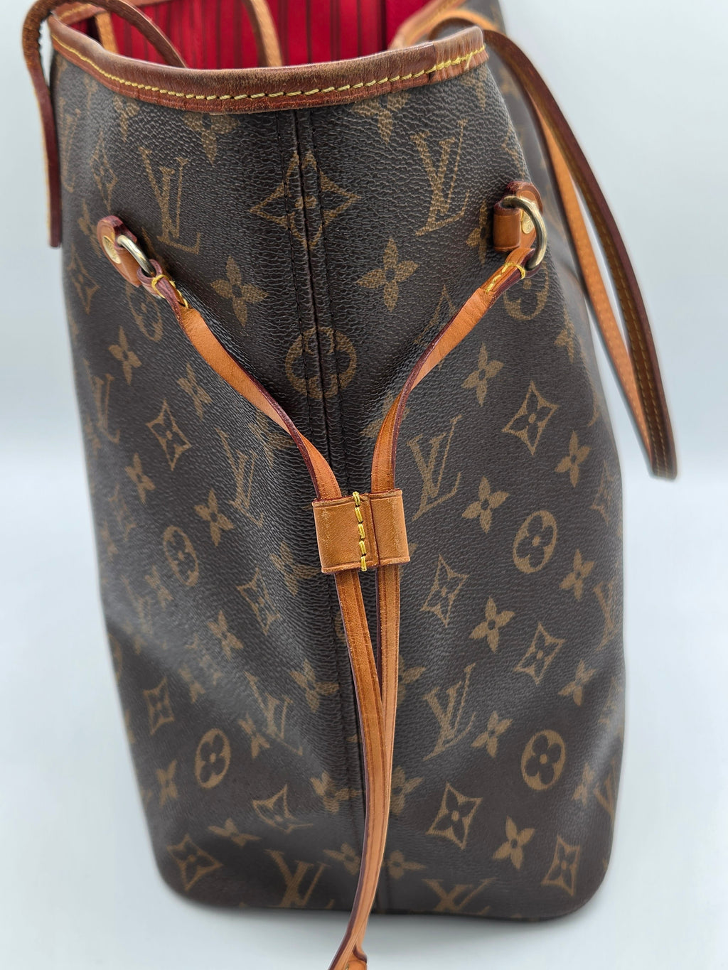 A Louis Vuitton monogram canvas tote bag with brown leather trim and drawstring details, shown against a light gray background.