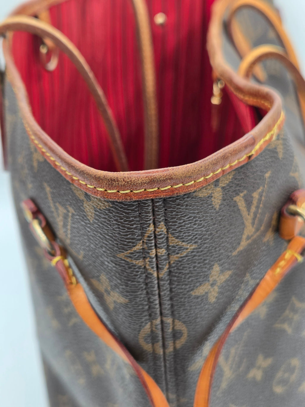 Close-up of a Louis Vuitton monogram canvas handbag showing the brown coated canvas exterior, tan leather trim, and a bright red interior lining.