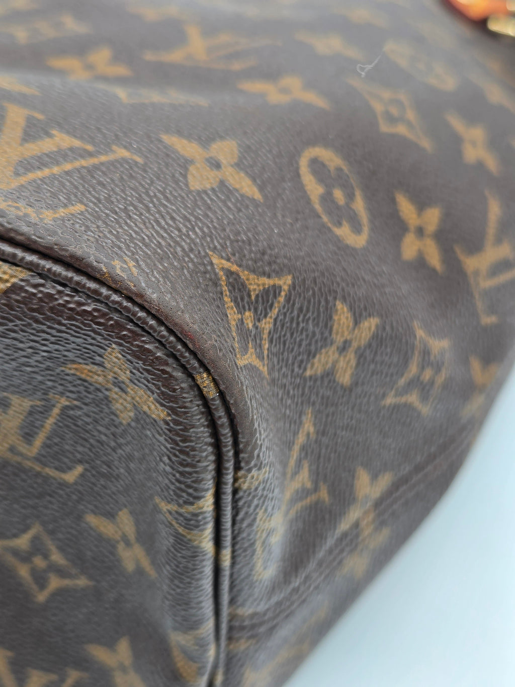 Close-up of a Louis Vuitton monogram canvas bag in dark brown with tan monogram patterns, showing the textured leather and a curved seam.